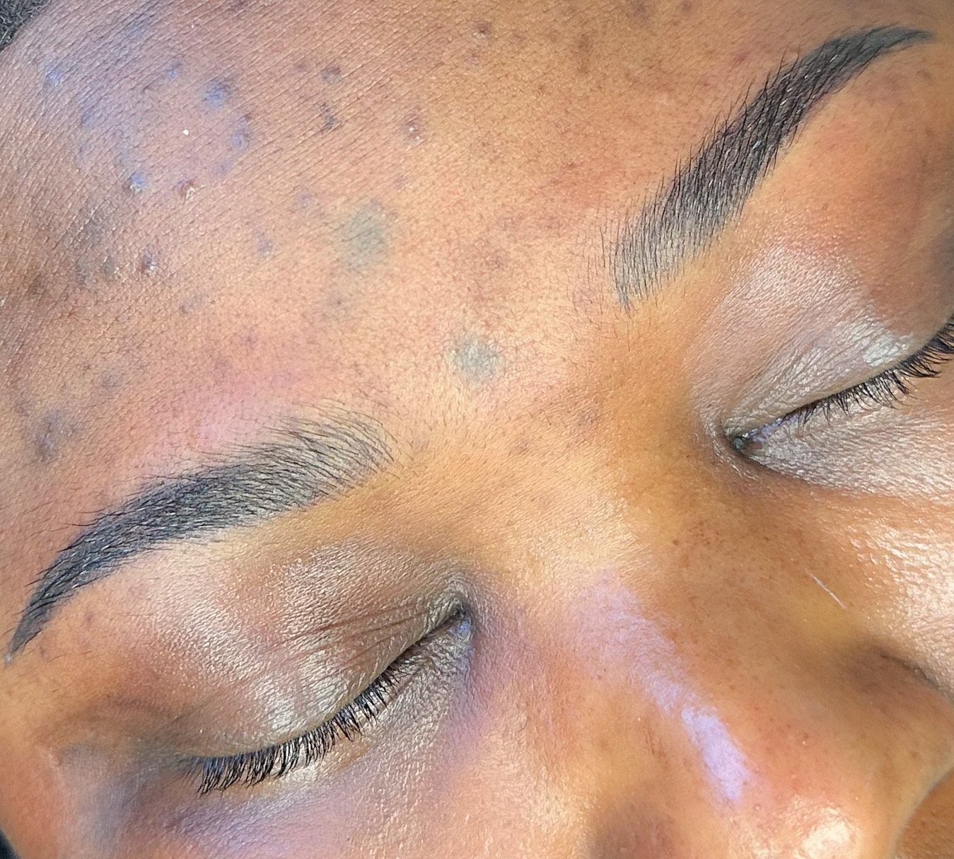 Close-up of a person's face focusing on closed eyes, with well-groomed eyebrows and subtle makeup on eyelids.