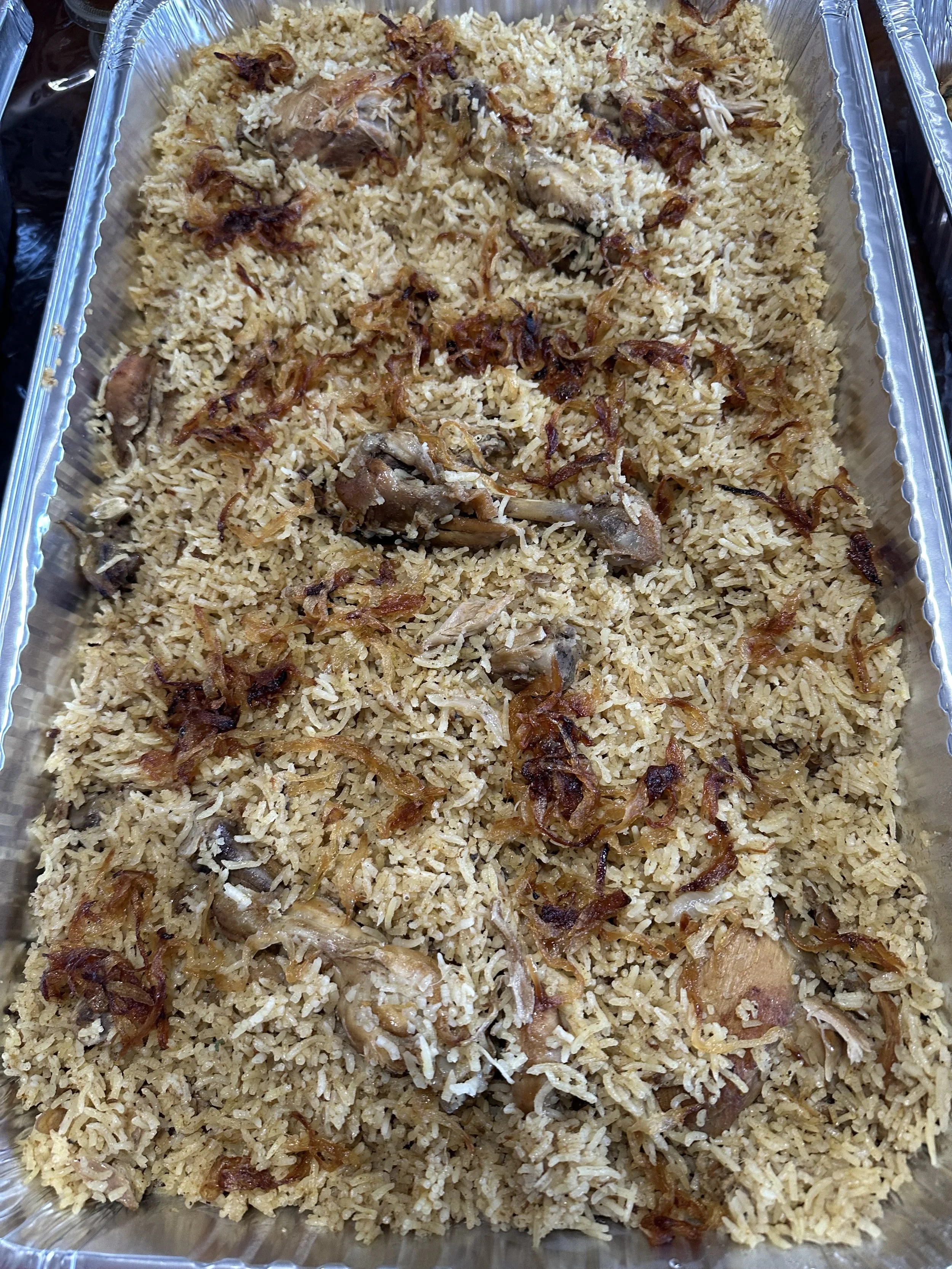 Chicken biryani topped with browned onions, served in a large foil catering tray.