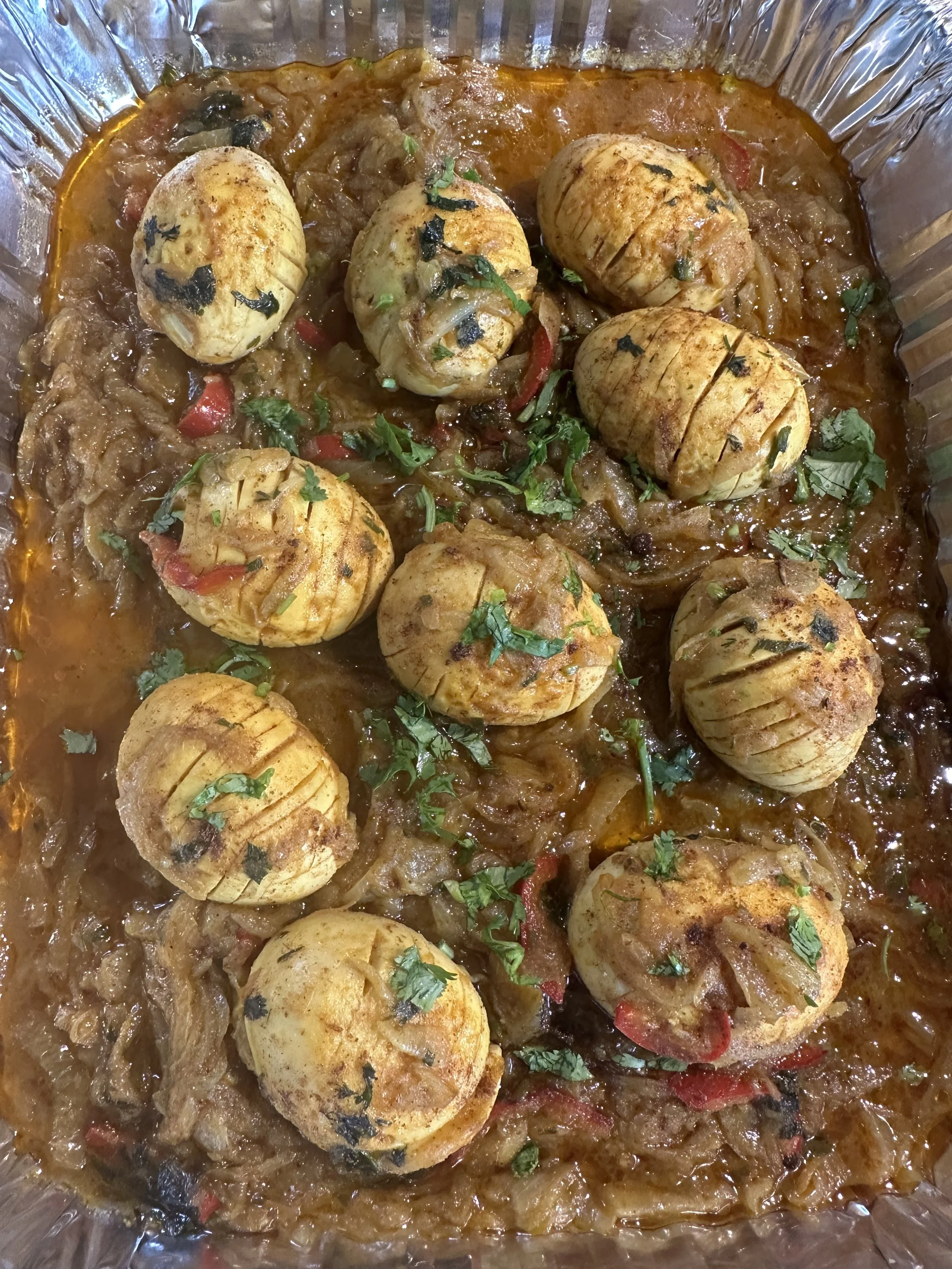 Bengali egg bhuna with whole eggs in thick onion gravy, garnished with cilantro in a foil catering tray.