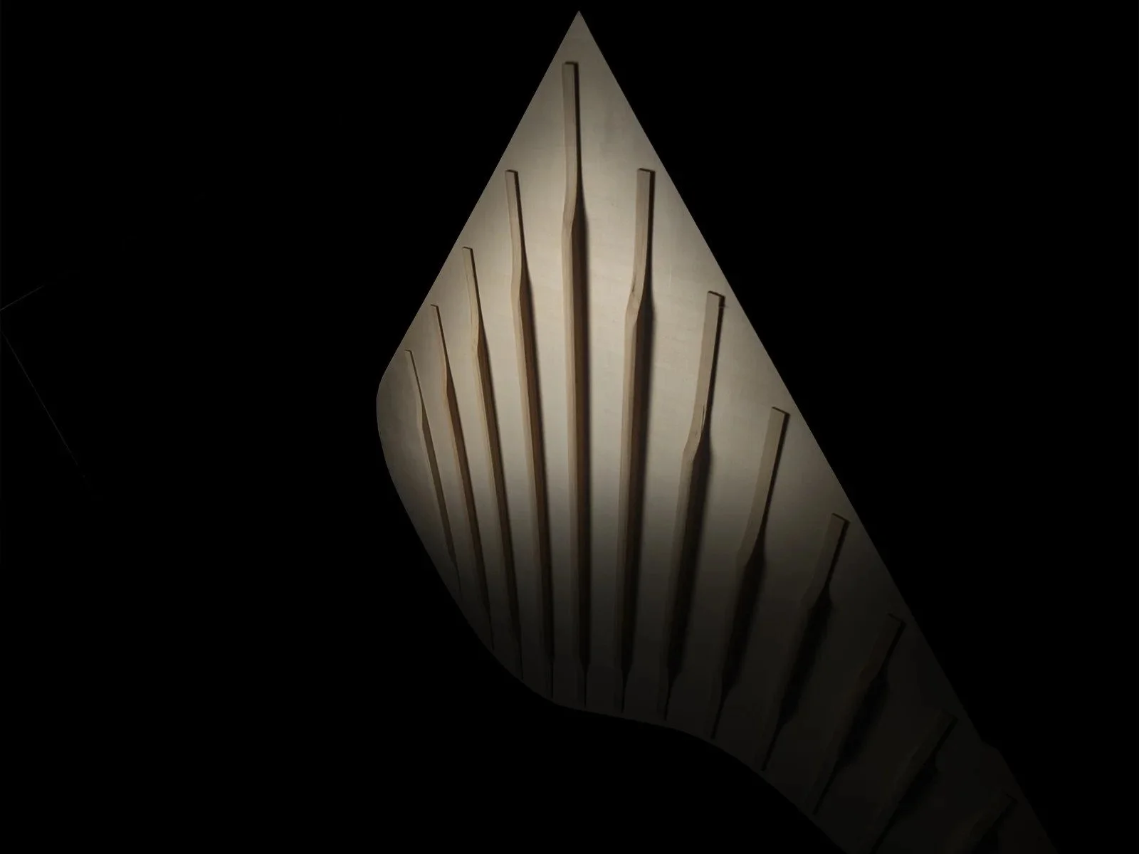 Abstract sculpture resembling a stylized leaf with sharp edges against a dark background.