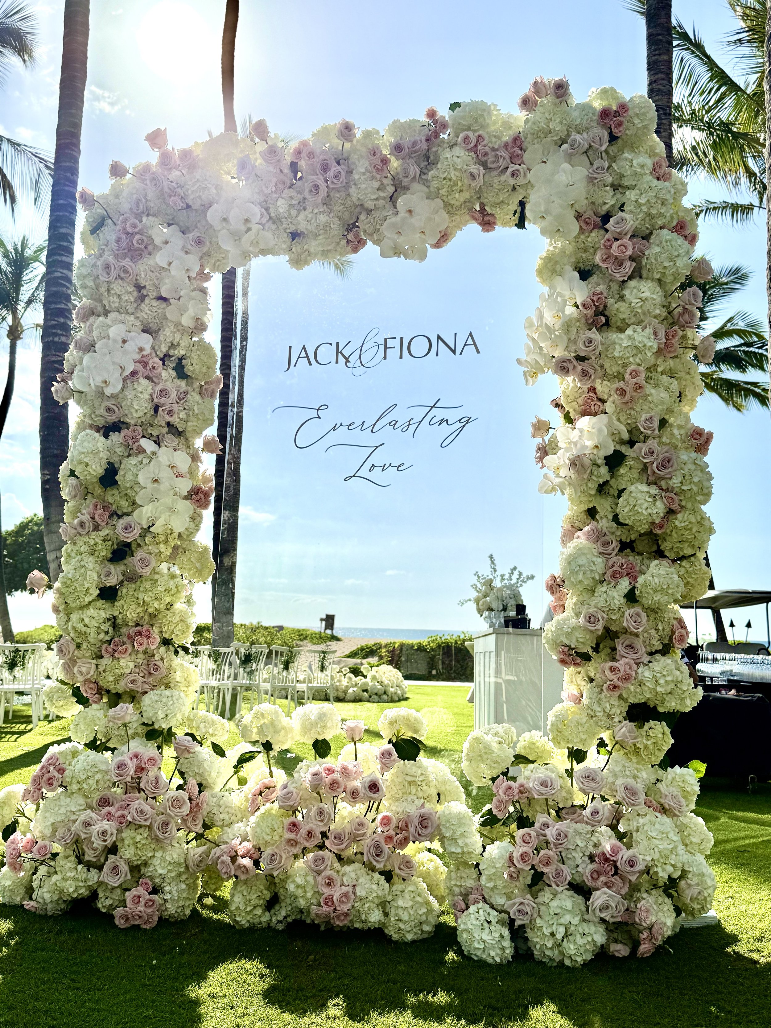 Large clear acrylic sign surrounded by flowers for wedding in Kona