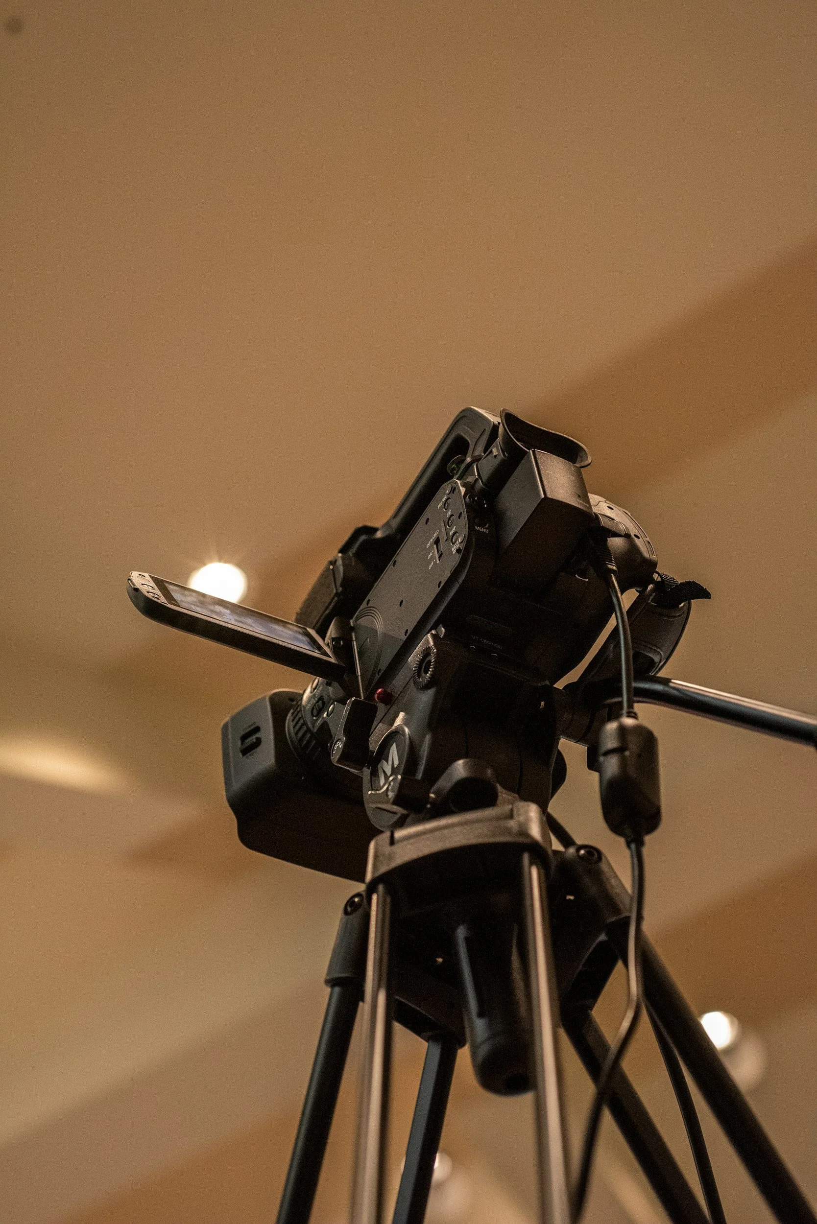 A professional camera mounted on a tripod, with a phone attached to its side, in an indoor setting.