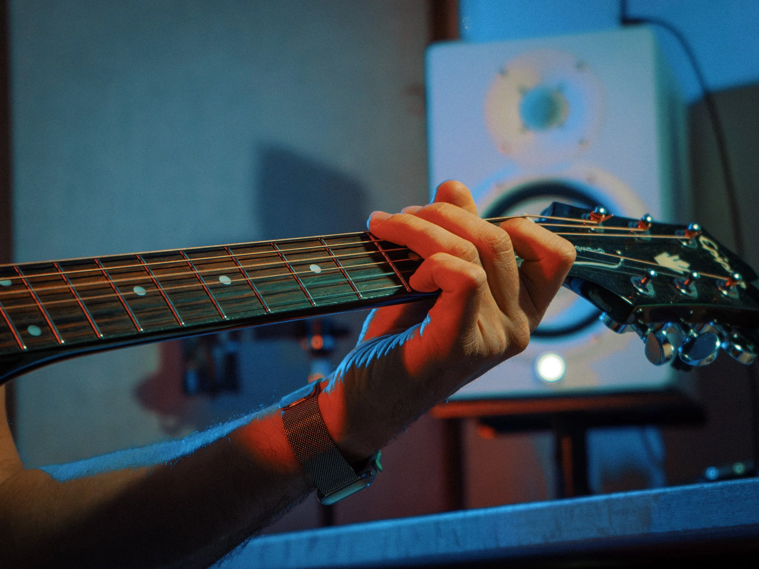 Main jouant de la guitare électrique dans une pièce faiblement éclairée avec un écran vidéo en arrière-plan.