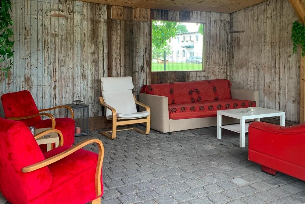  Gemütlicher, überdachter Außen-Loungebereich mit rustikalen Holzwänden, roten Sesseln und einem Sofa. Ein idealer Workshop Space für entspannte Pausen. 