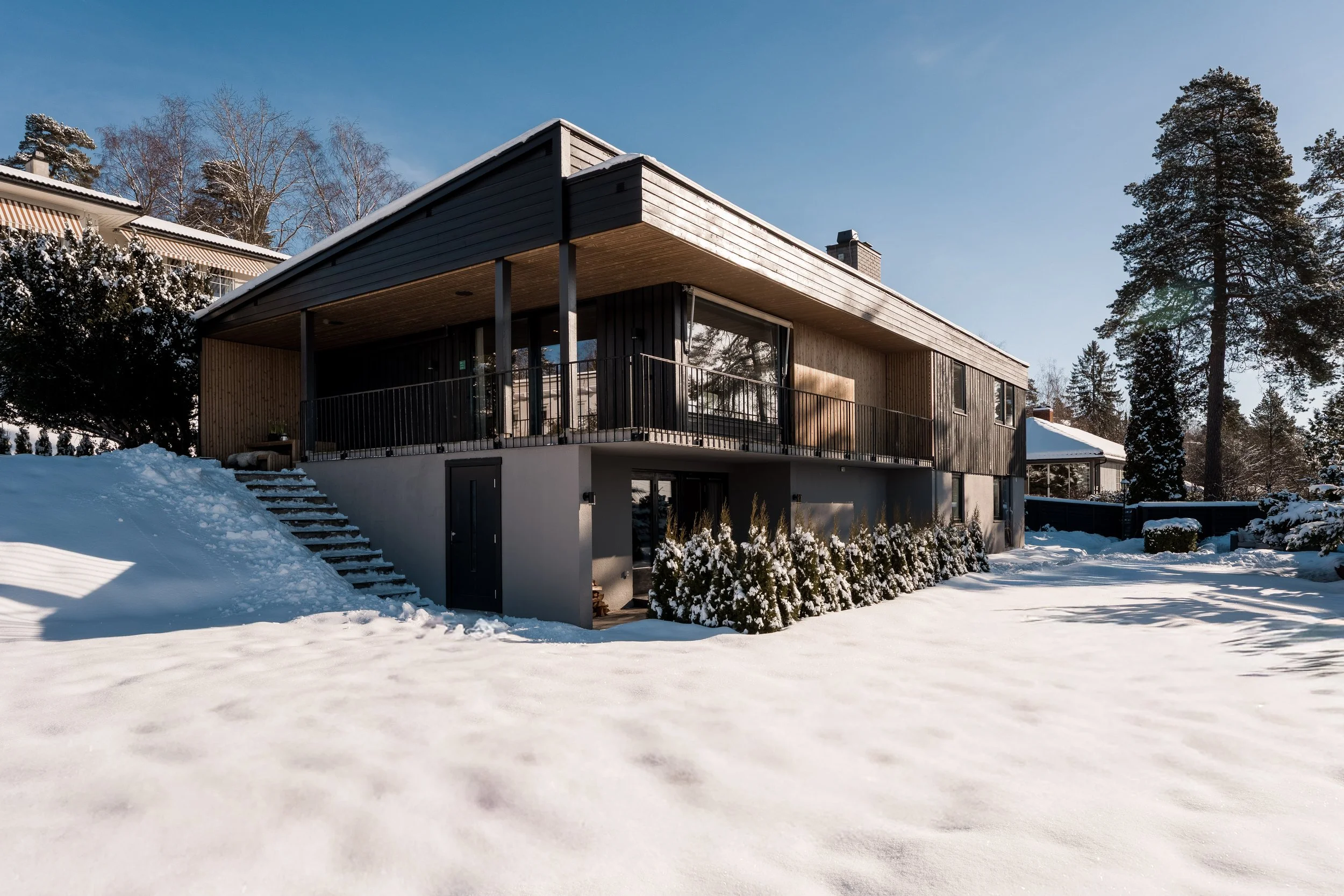 Moderne hus med utendørs balkong, omgitt av snø og bjørketrær på vinteren.