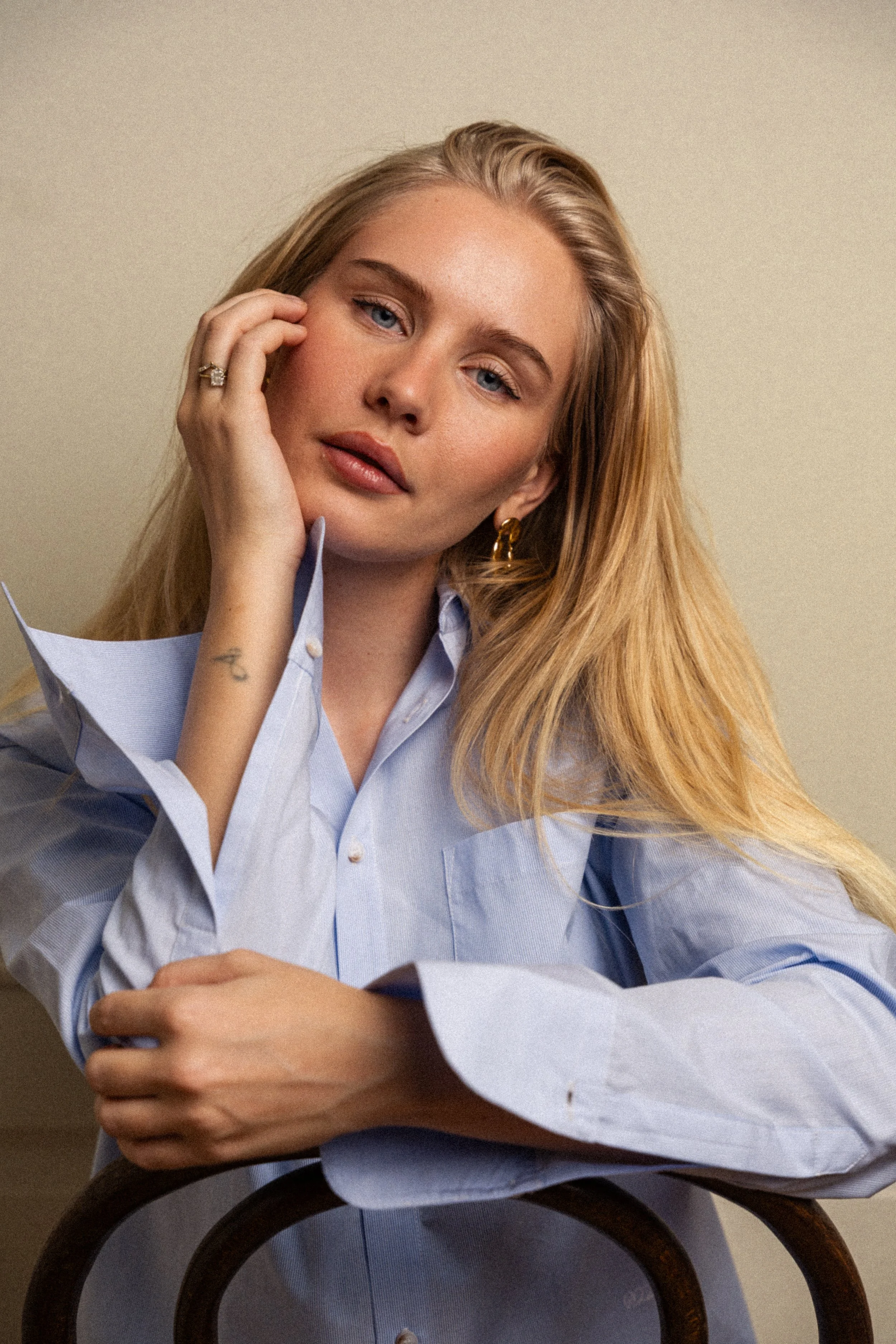Portrett av en ung kvinne med blond hår, blå øyne, iført lyseblå skjorte, sett foran en nøytral bakgrunn.