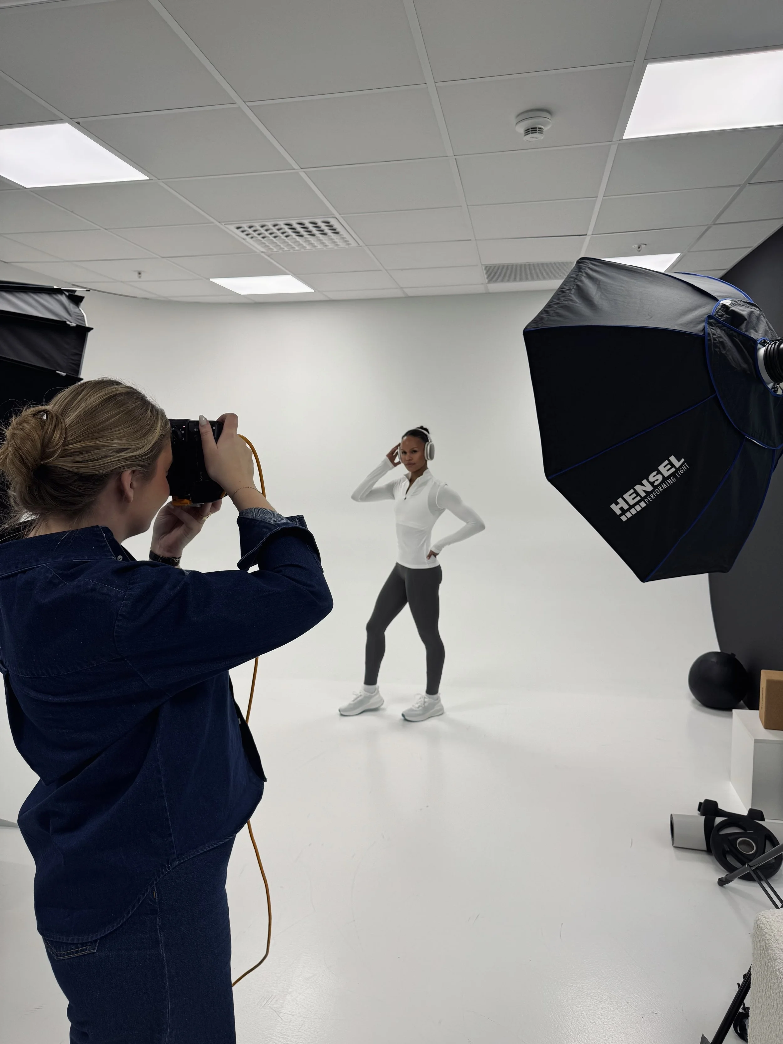 En kvinne poserer for en fotoshoot i et studio med profesjonelt lysutstyr, mens en fotograf tar bilder av henne.