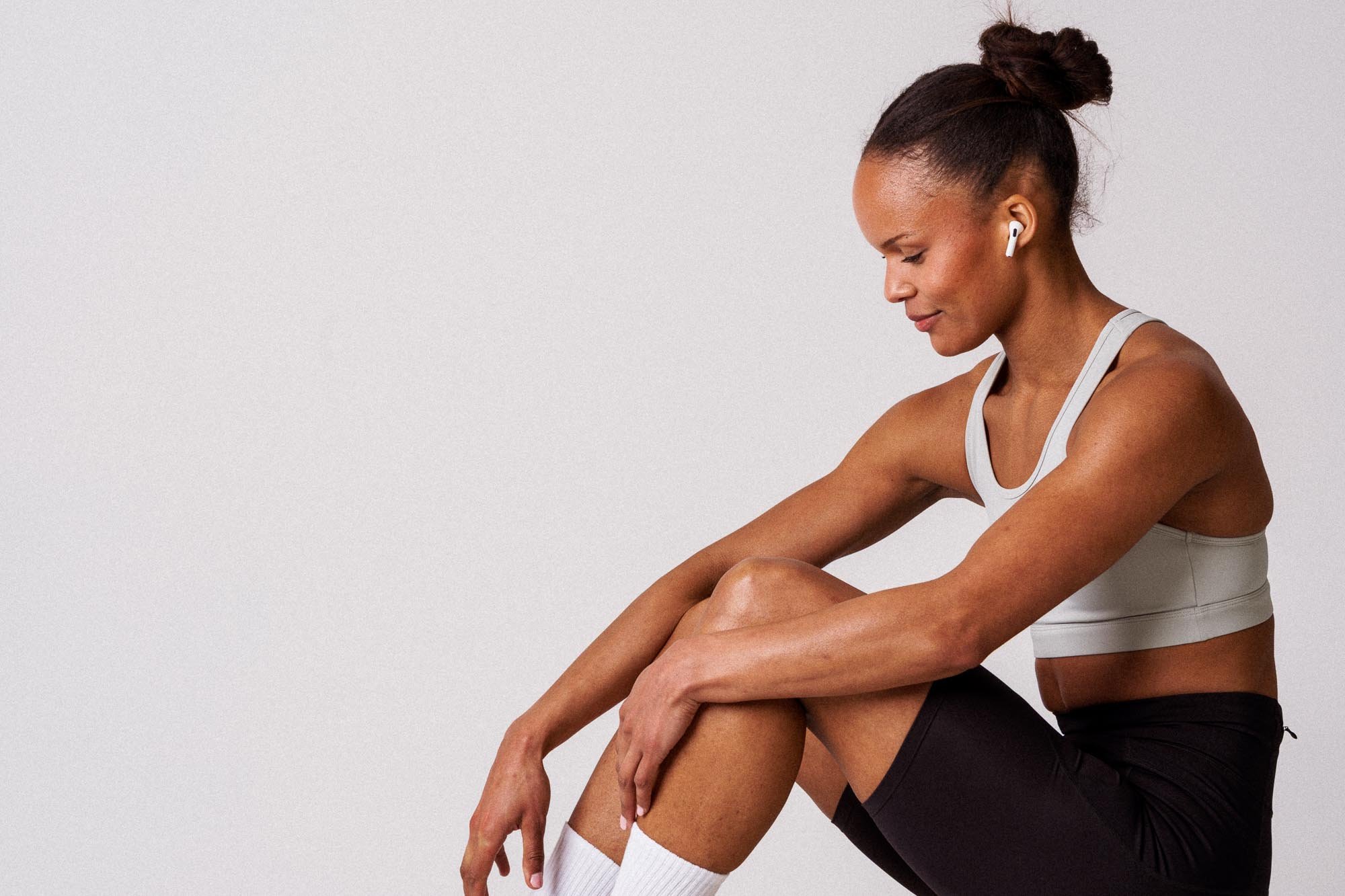 Kvinne i treningsklær med høreplugger som sitter på gulvet og slapper av.