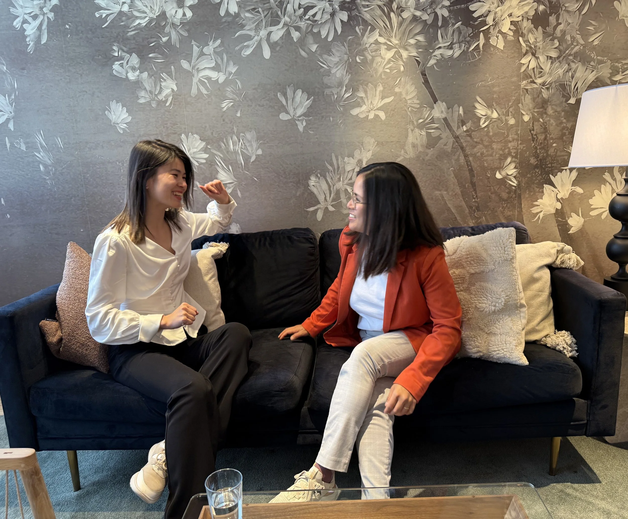 Two east asian women sitting on a couch and laughing