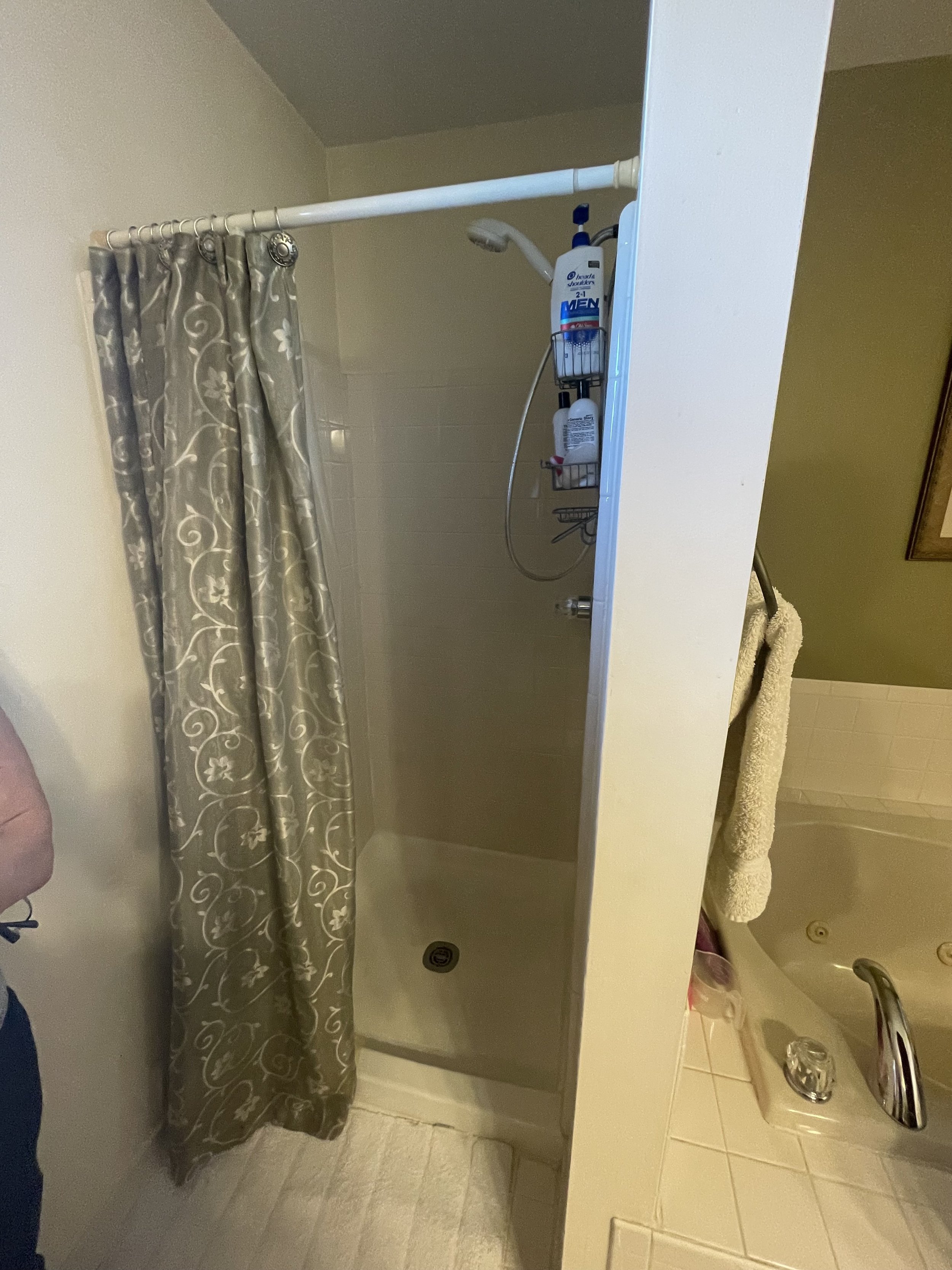 A small shower stall with a beige curtain, a white showerhead, and a wall-mounted rack holding bottles of shampoo and body wash.