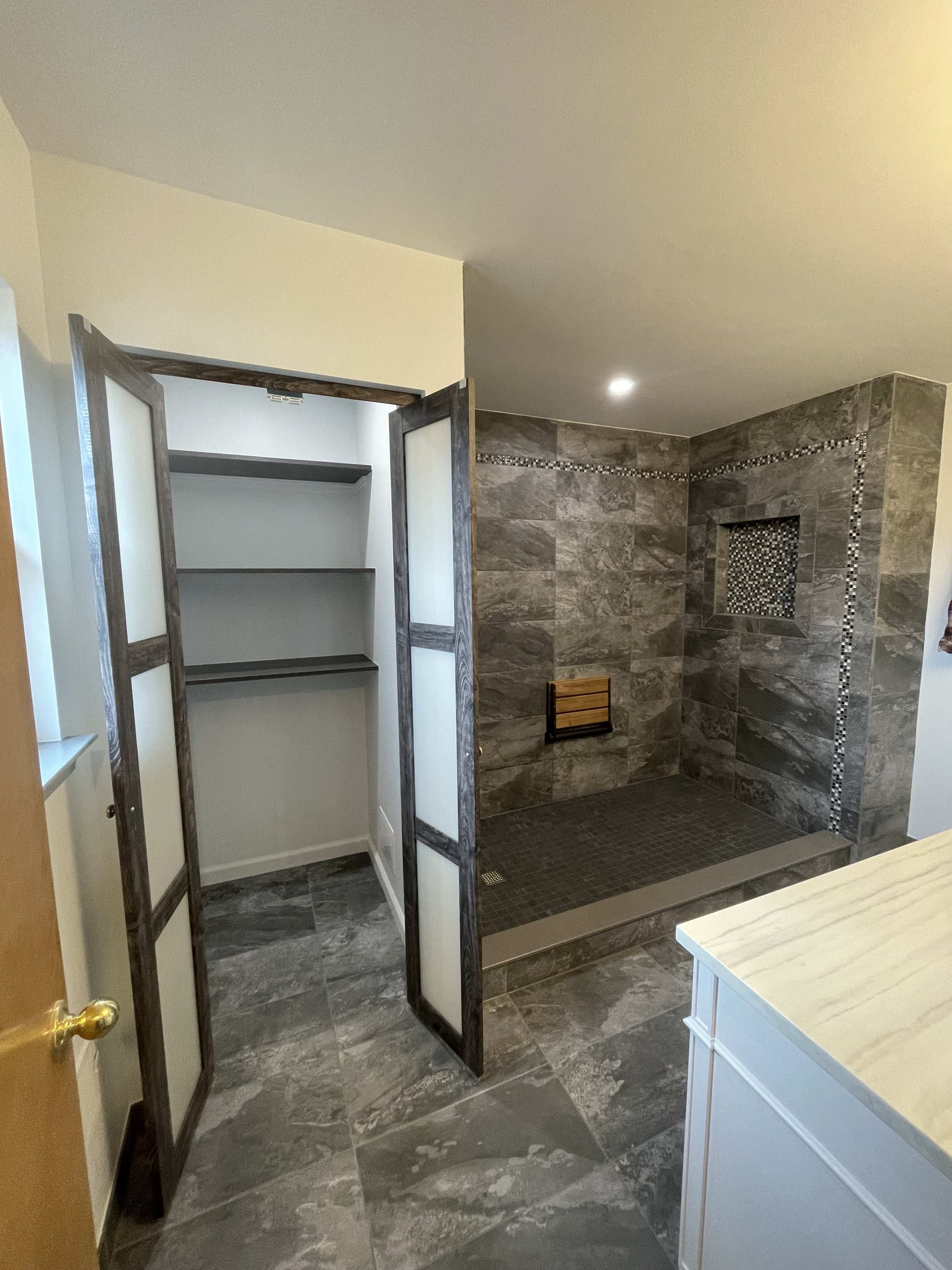 Bathroom with a walk-in shower and a closet door open revealing shelves.