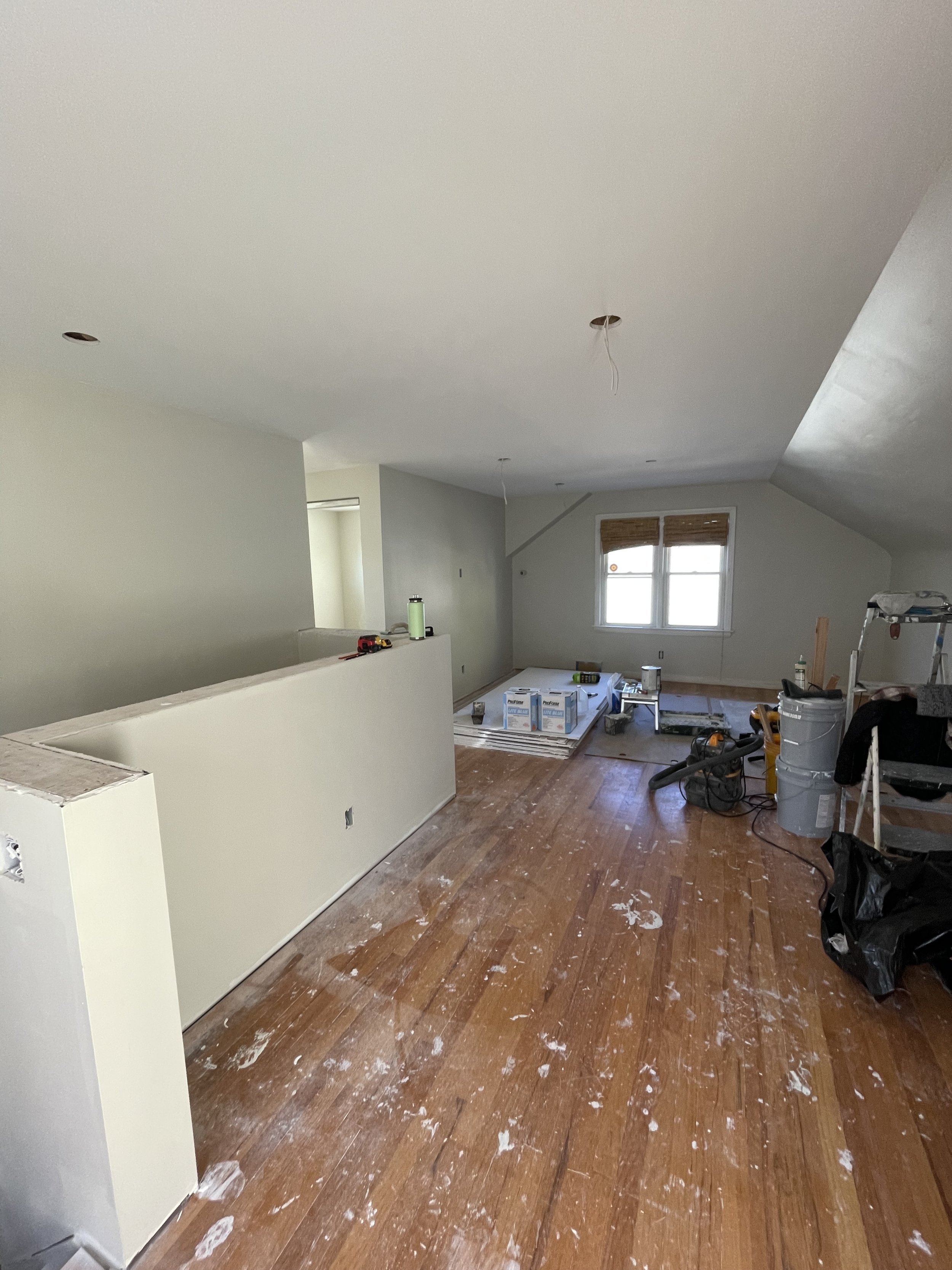 Room under renovation with construction tools, supplies, and paint splatters on hardwood floor.