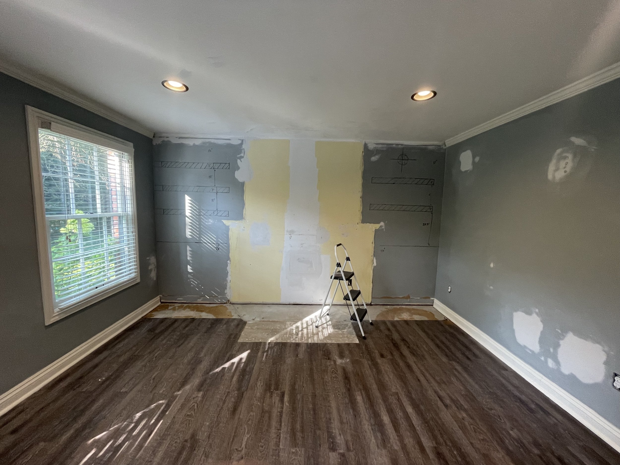 Room under renovation with drywall patches on the walls, a step ladder in the center, and a window on the left wall.