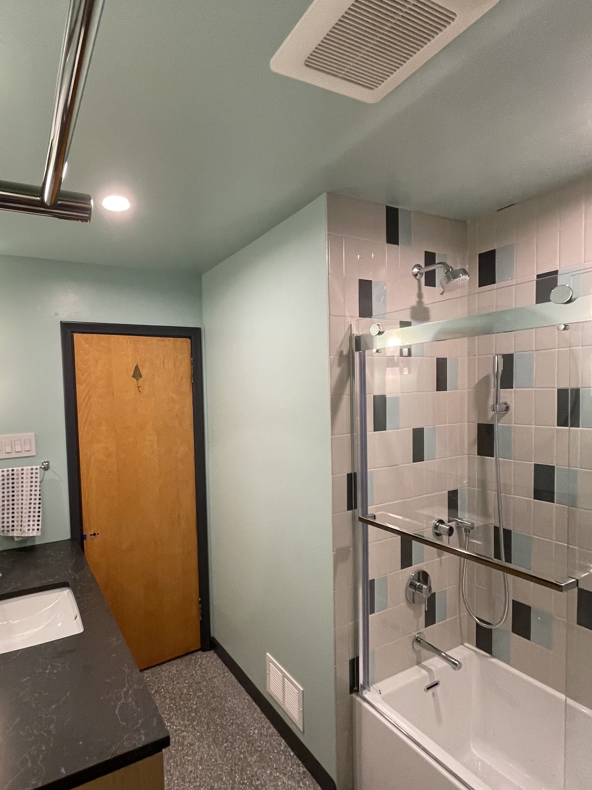 Part of a bathroom showing a wood door with a peephole, a bathtub with a glass shower enclosure, and a mint green wall.