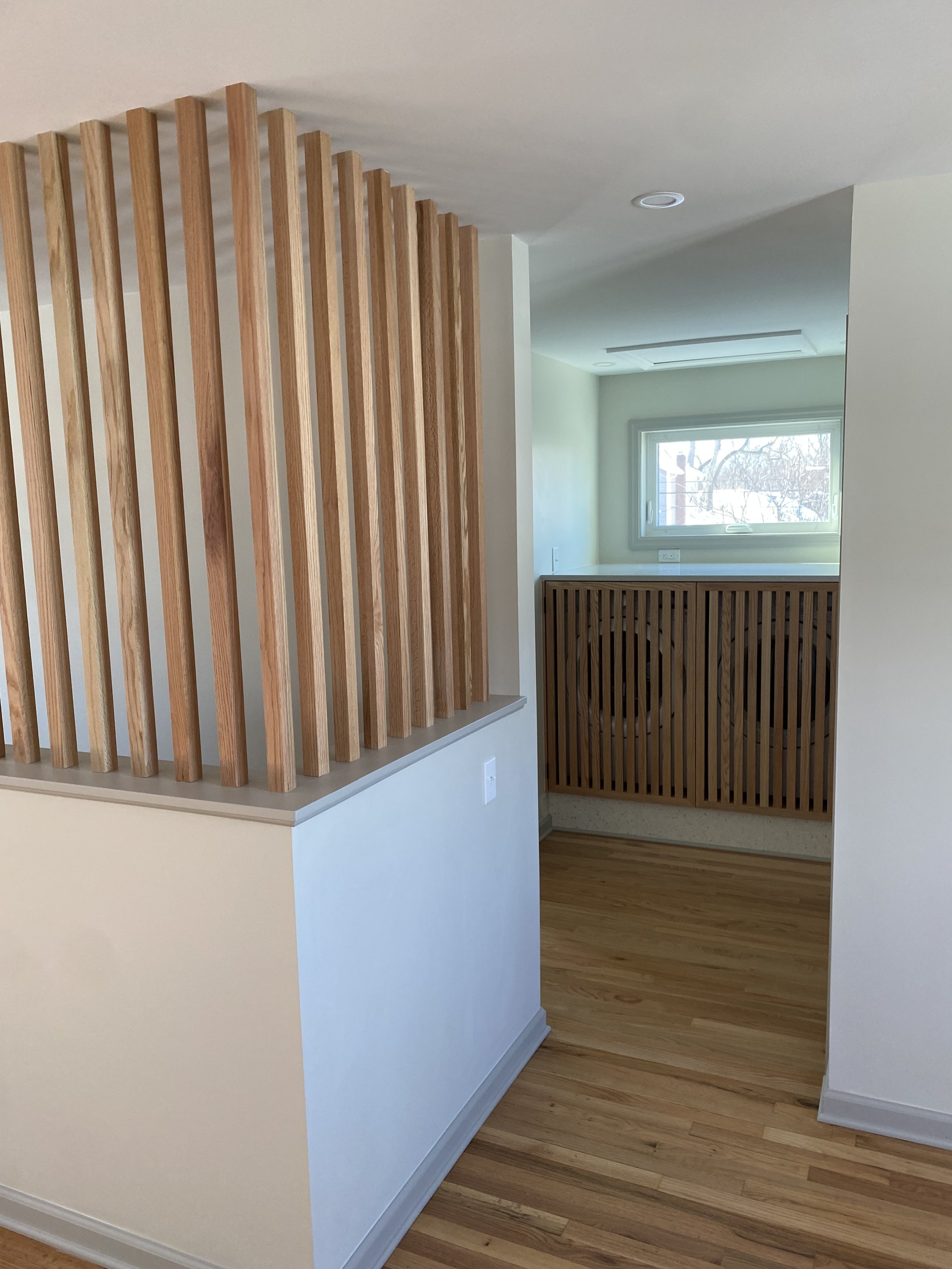 Interior view of a modern home with wood slat partitions, hardwood floors, and a small window letting in natural light.