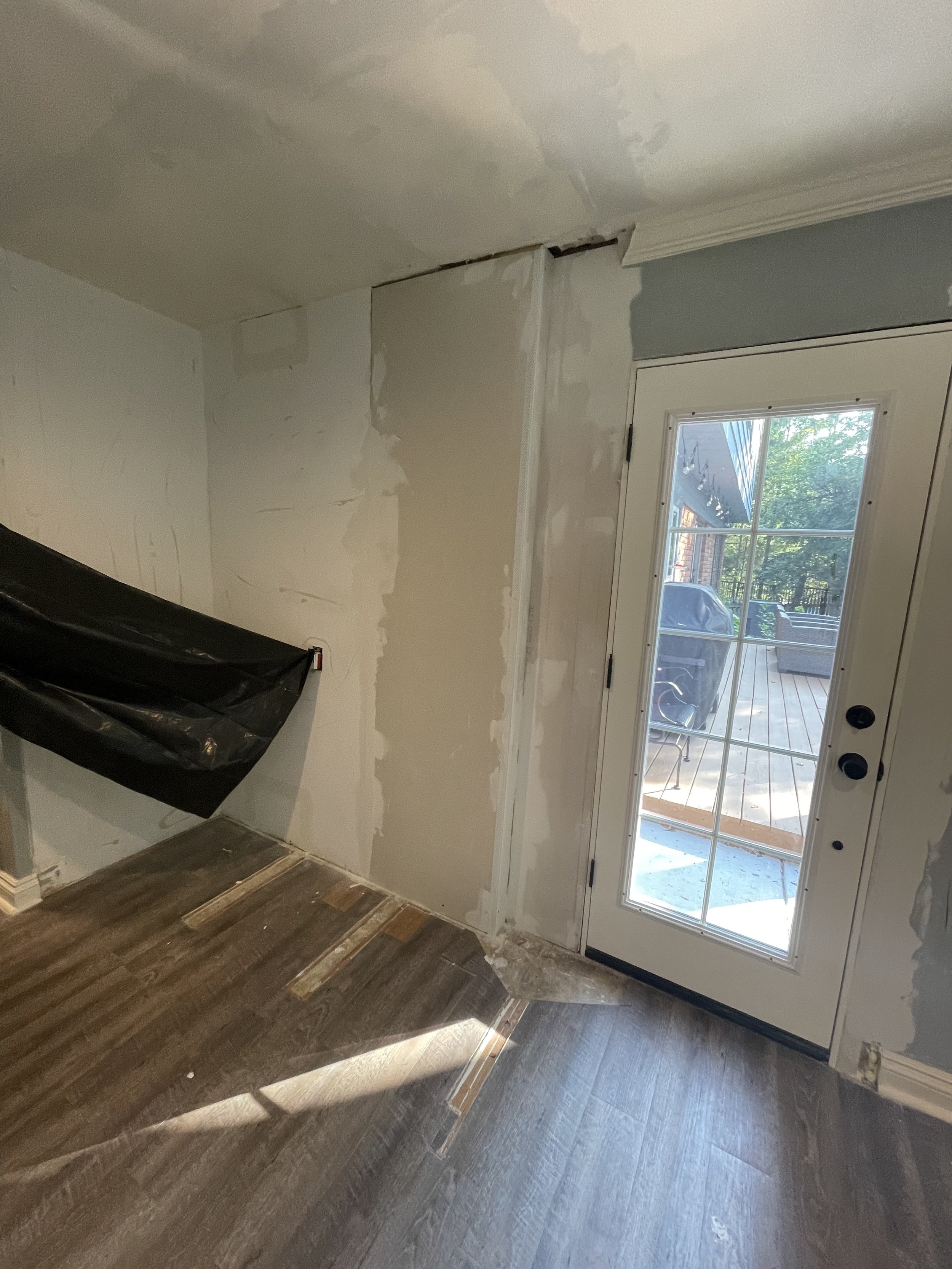Interior room under renovation with a partially painted wall, a glass door leading outside, and a floor with visible repair areas.