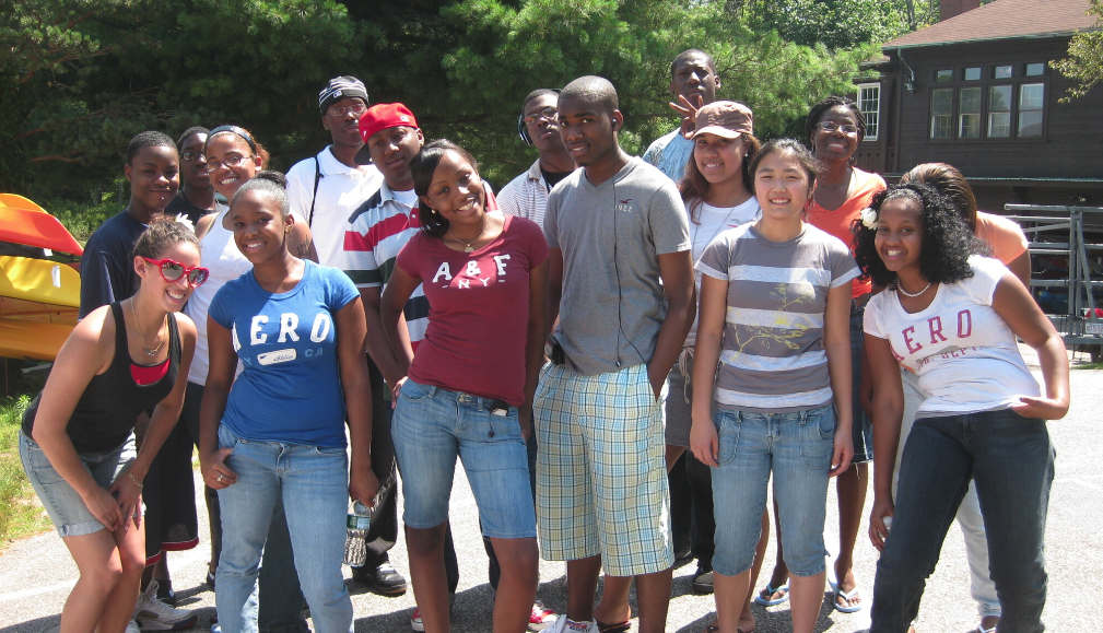 A diverse group of teenagers outdoors, smiling and posing for a photo on a sunny day.