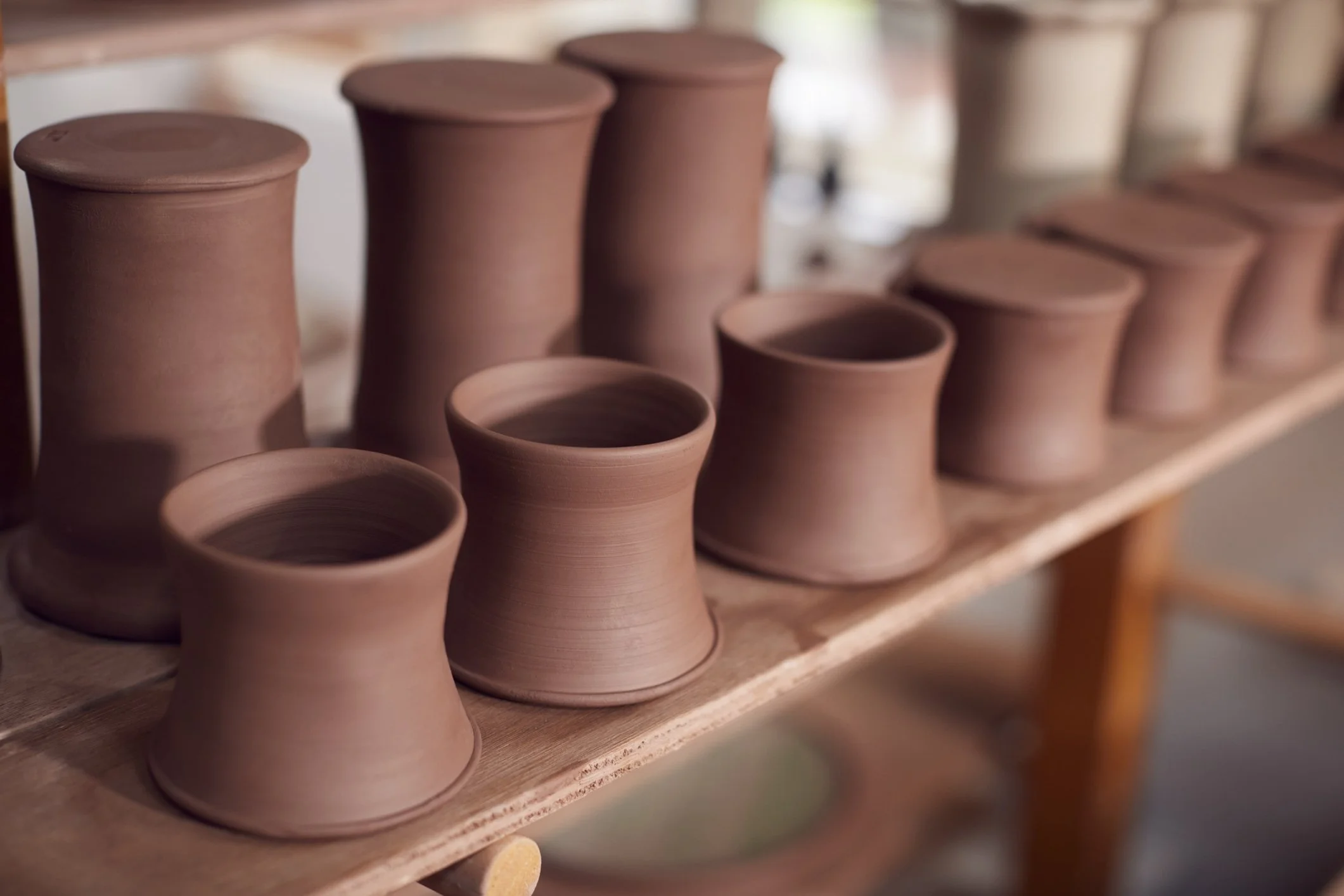 Several plain terracotta pots arranged on a wooden shelf in a pottery studio drying, ready to be fired in the kiln.