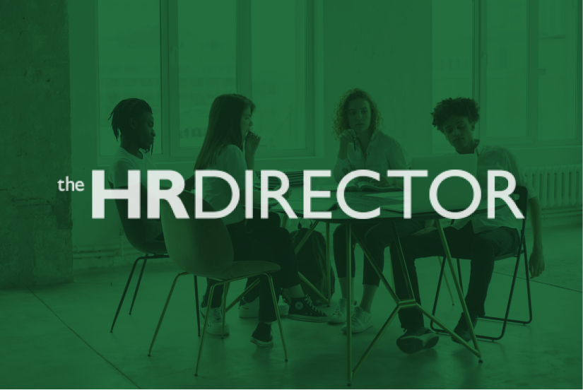 Group of four people sitting around a table with a book, in a room with large windows and natural lighting.