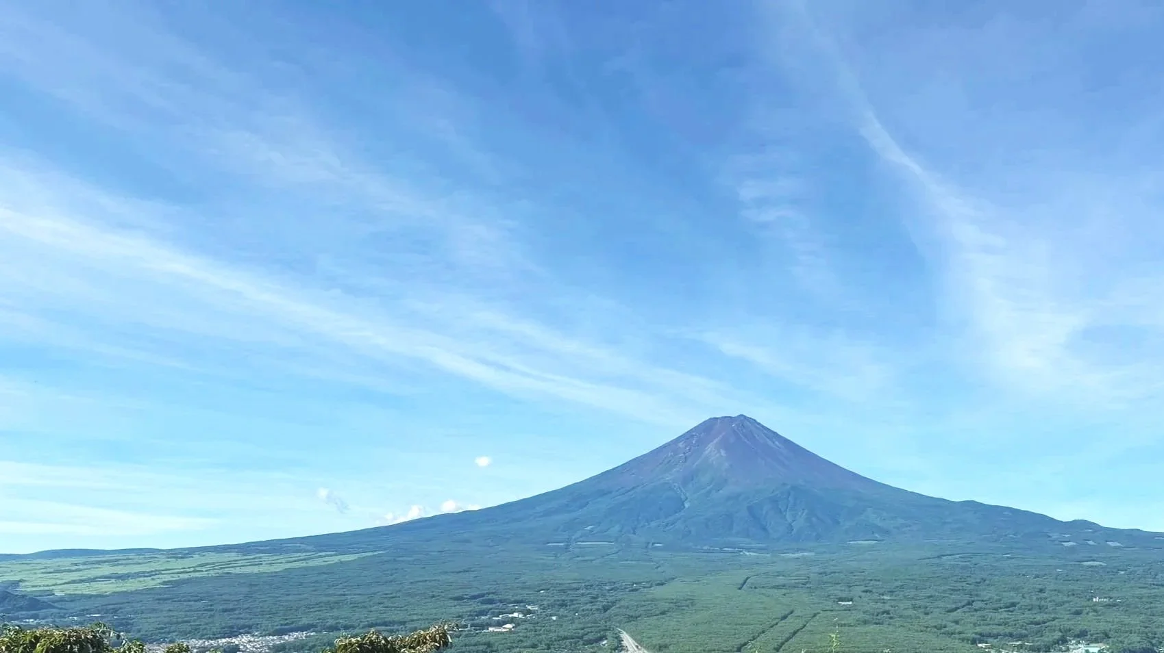 A volcanic mountain with a conical shape and a snow-capped summit under a blue sky with wispy clouds.