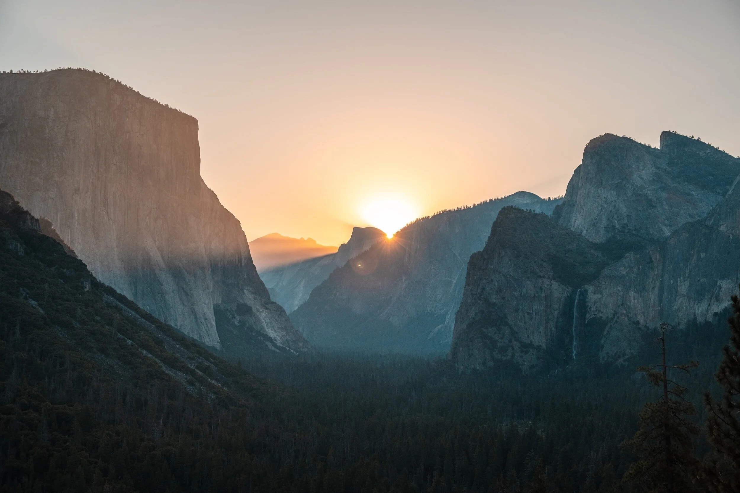 Sunrise over mountainous landscape with cliffs and forested slopes.