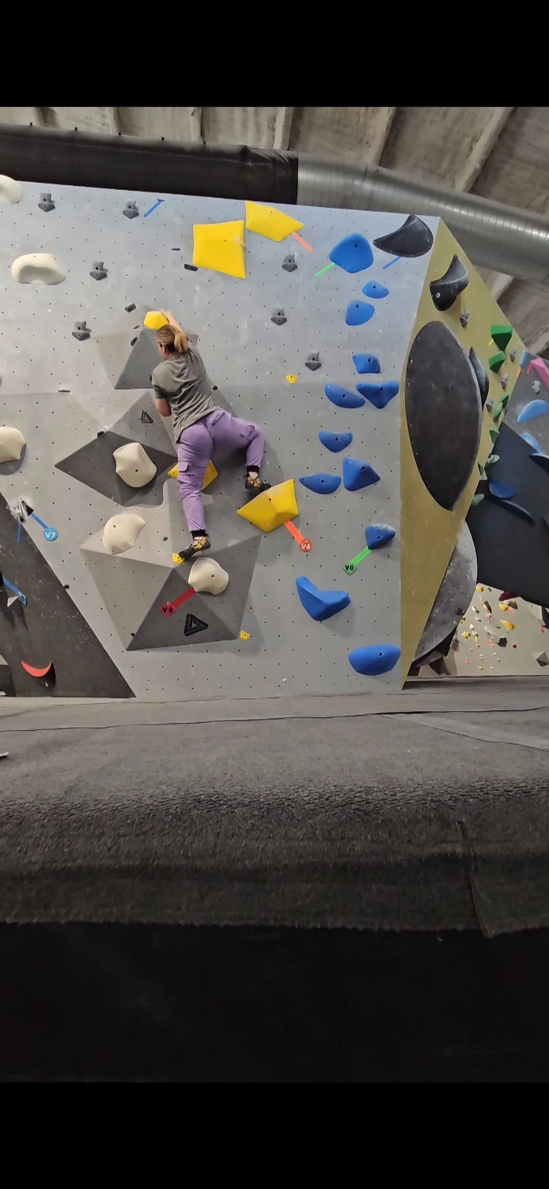Person climbing an indoor bouldering wall with various colored holds.