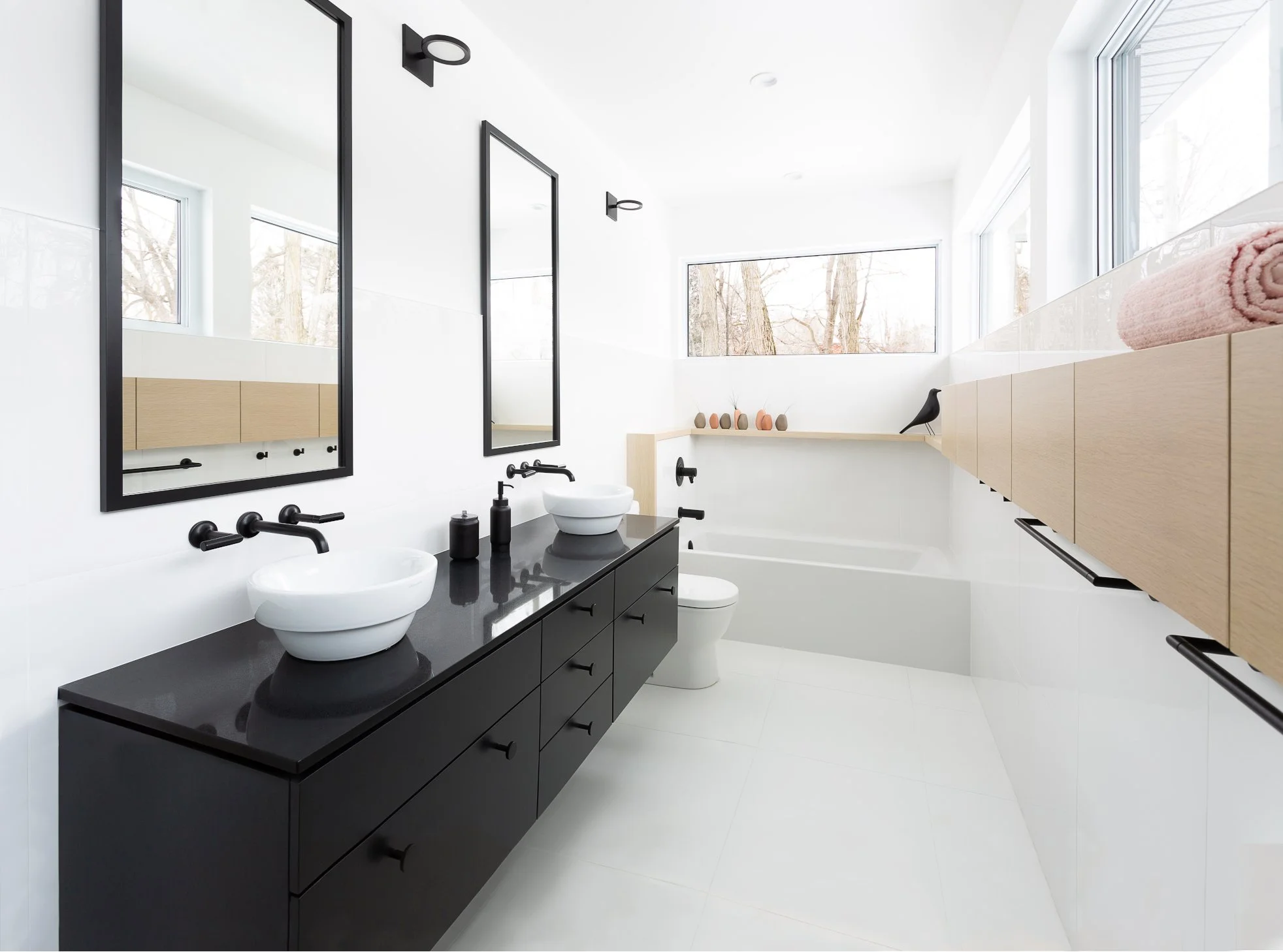 Modern bathroom with double sinks, black vanity, large mirrors, white bathtub, wooden storage cabinets, and black fixtures.
