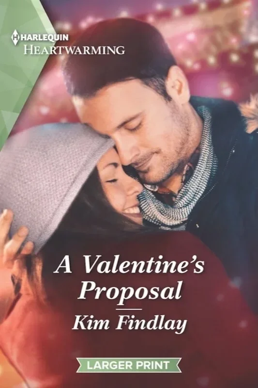 Cover art for author Kim Findlay’s romance novel “A Valentine’s Proposal.” A young couple in a gentle embrace are outdoors wearing winter clothes in a light snow.  In the background is a blurred image of valentines winter fair colorful lighting
