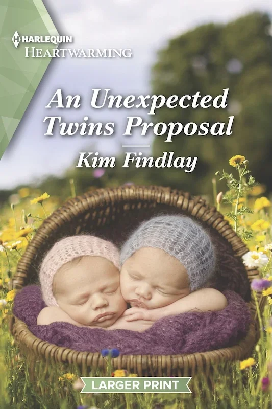 Cover art for author Kim Findlay’s romance novel “A Unexpected Twins Proposal.” Two Newborn babies wearing knitted caps are arranged in a large basket in a field in spring