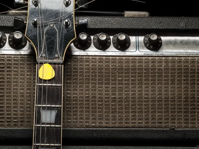 closeup of a gibson les paul guitar with a yellow pick in the strings, leaning against a silverface Fender amplifier