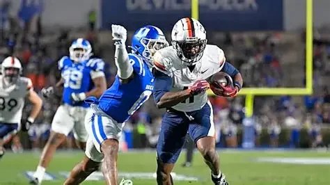 An American football player in a white jersey running with the ball, attempting to evade a defender in a blue jersey during a game.