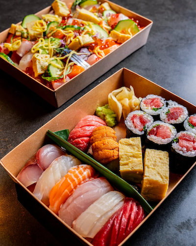 Two premium Japanese bento boxes from Kōsen in Tampa are displayed on a dark surface. The foreground box features an assortment of fresh nigiri.