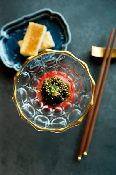 A luxurious serving of black caviar topped with gold leaf in a gold-rimmed crystal glass, with toasted brioche points visible in the background.