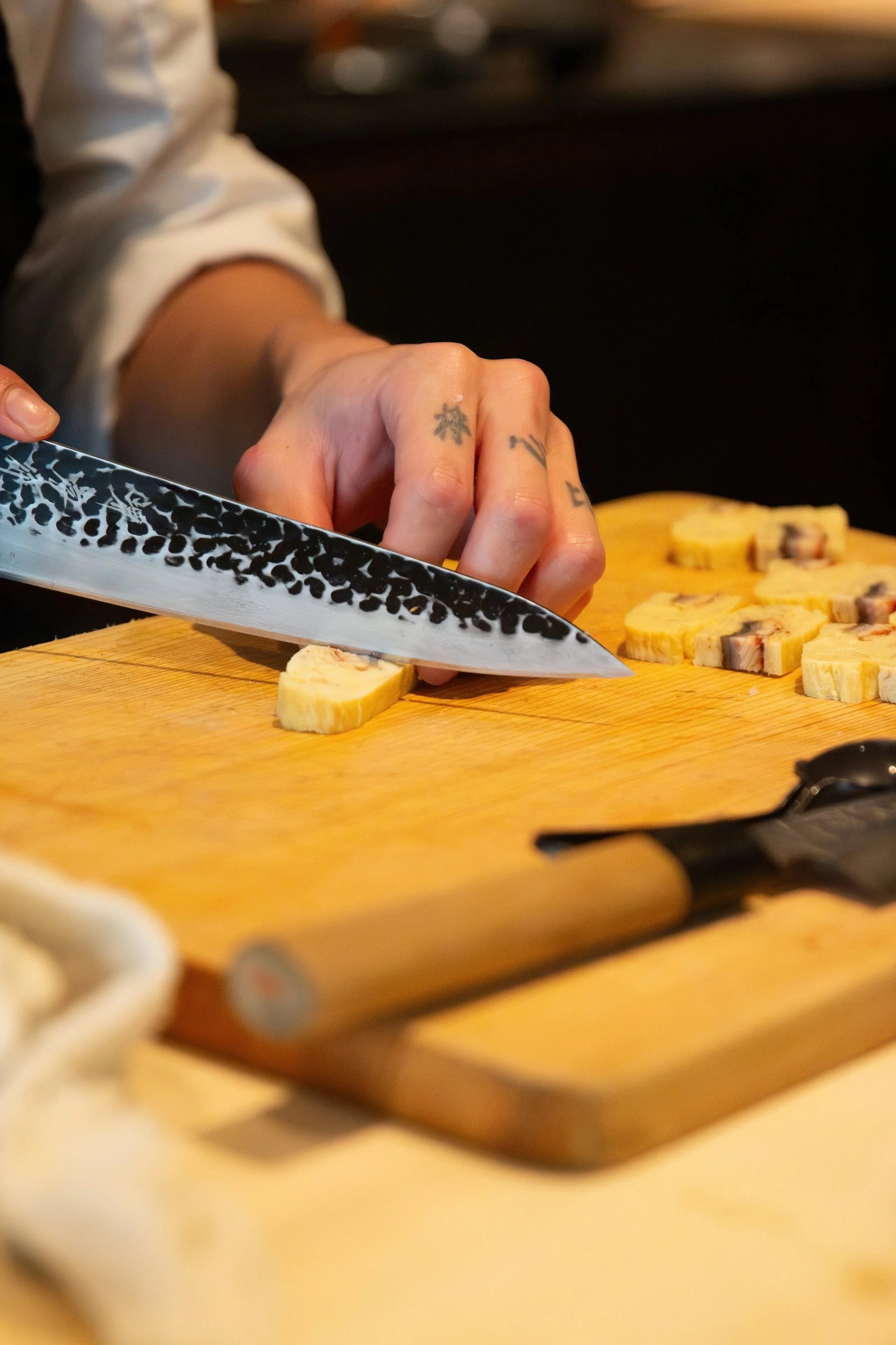 A person slicing a roll with a patterned knife on a wooden cutting board, with slices of a food item on the board in Kōsen in Tampa.