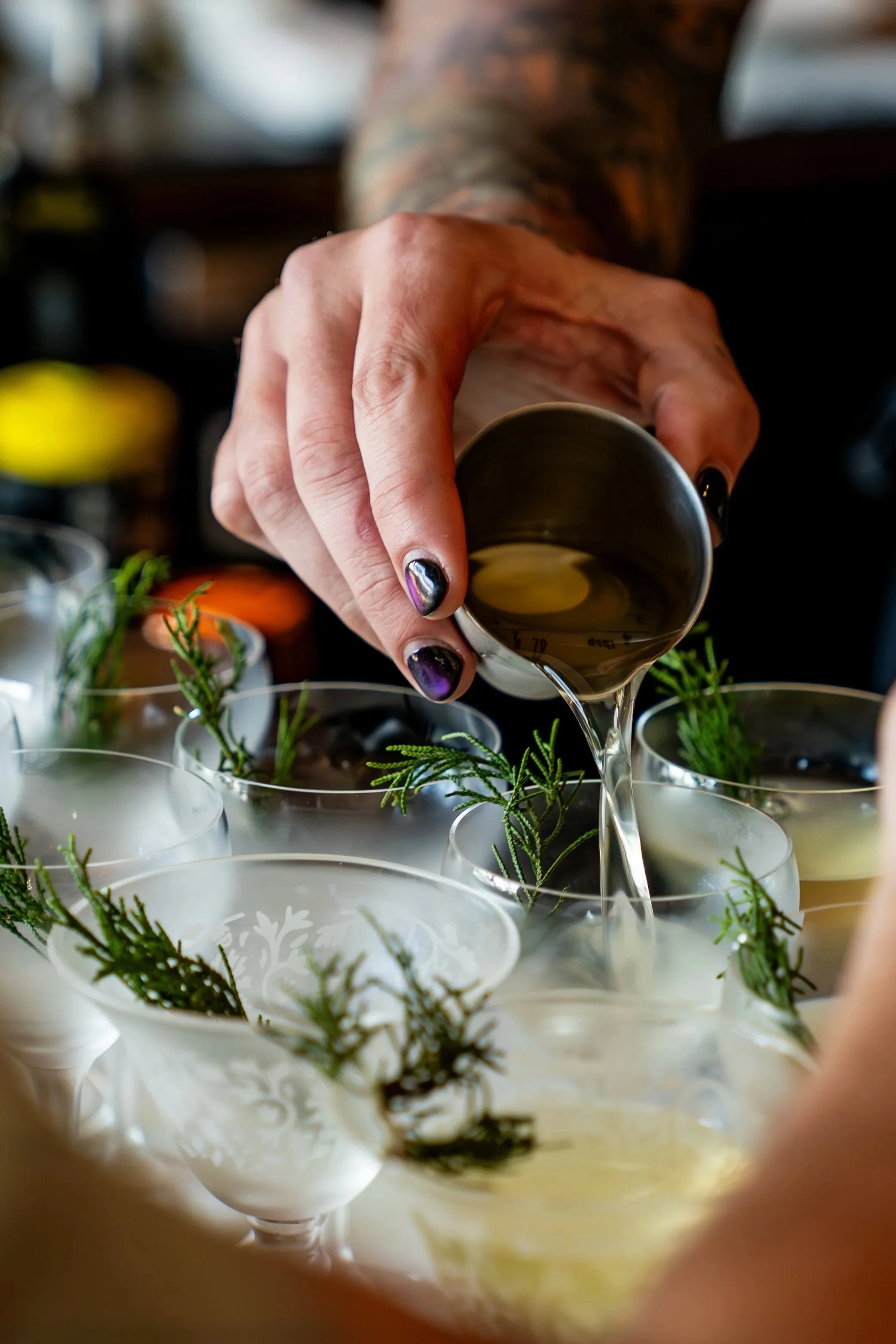 A close-up, action shot of a bartender at Kosen in Tampa precisely pouring a vibrant orange cocktail from a glass mixing pitcher into a chilled coupe glass.