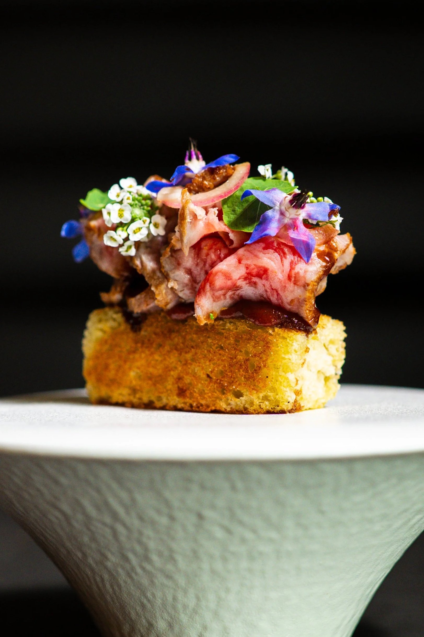 wagyu toast embellished with colorful flowers sitting atop a white dish