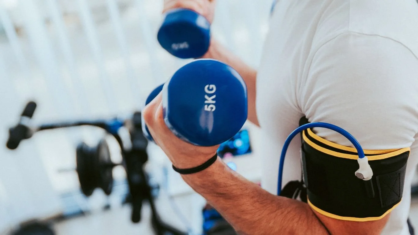 Someone lifting 5KG weights while they use blood flow restriction therapy.