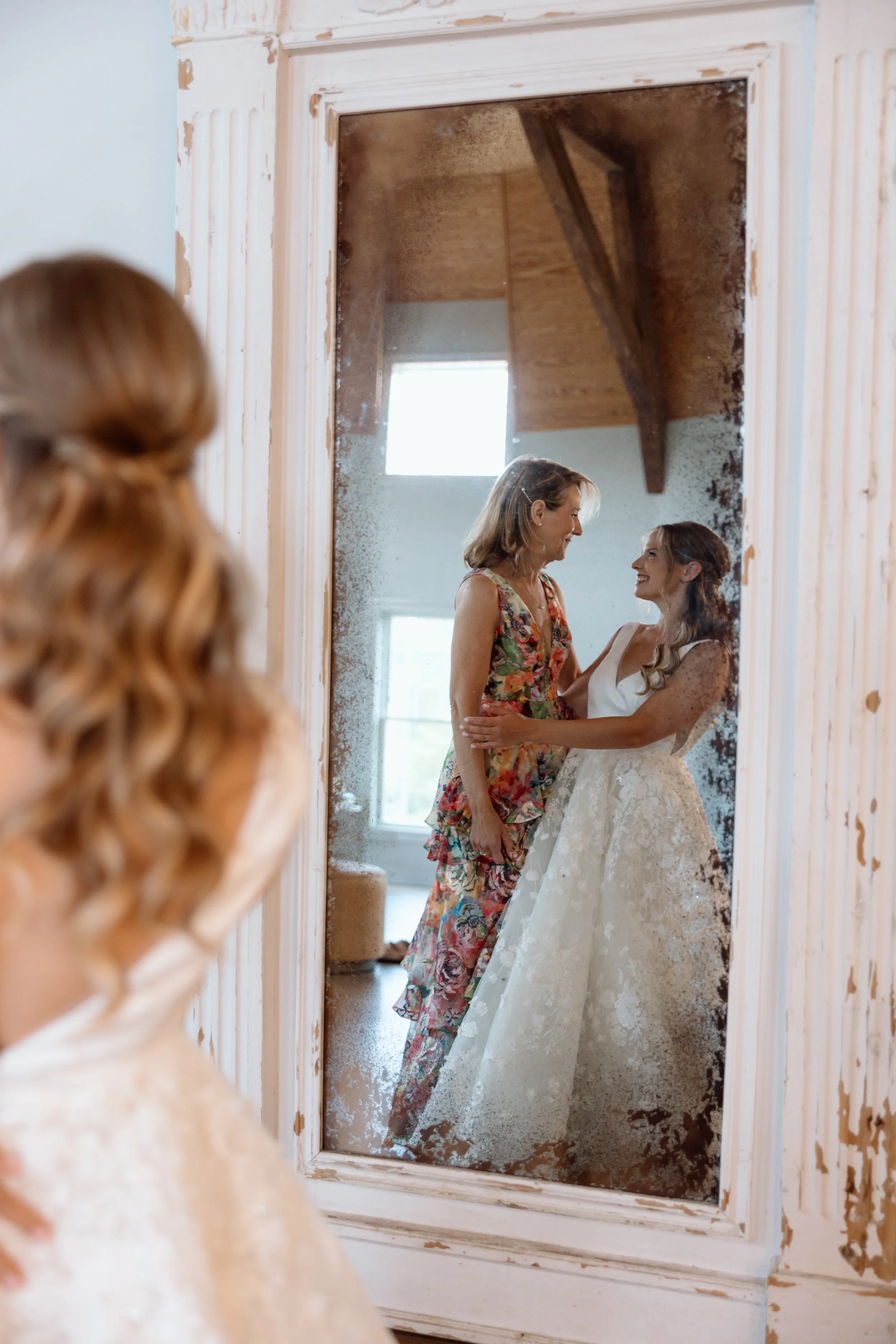 Bride and mother having a sentimental moment in front of mirror in bridal suite.