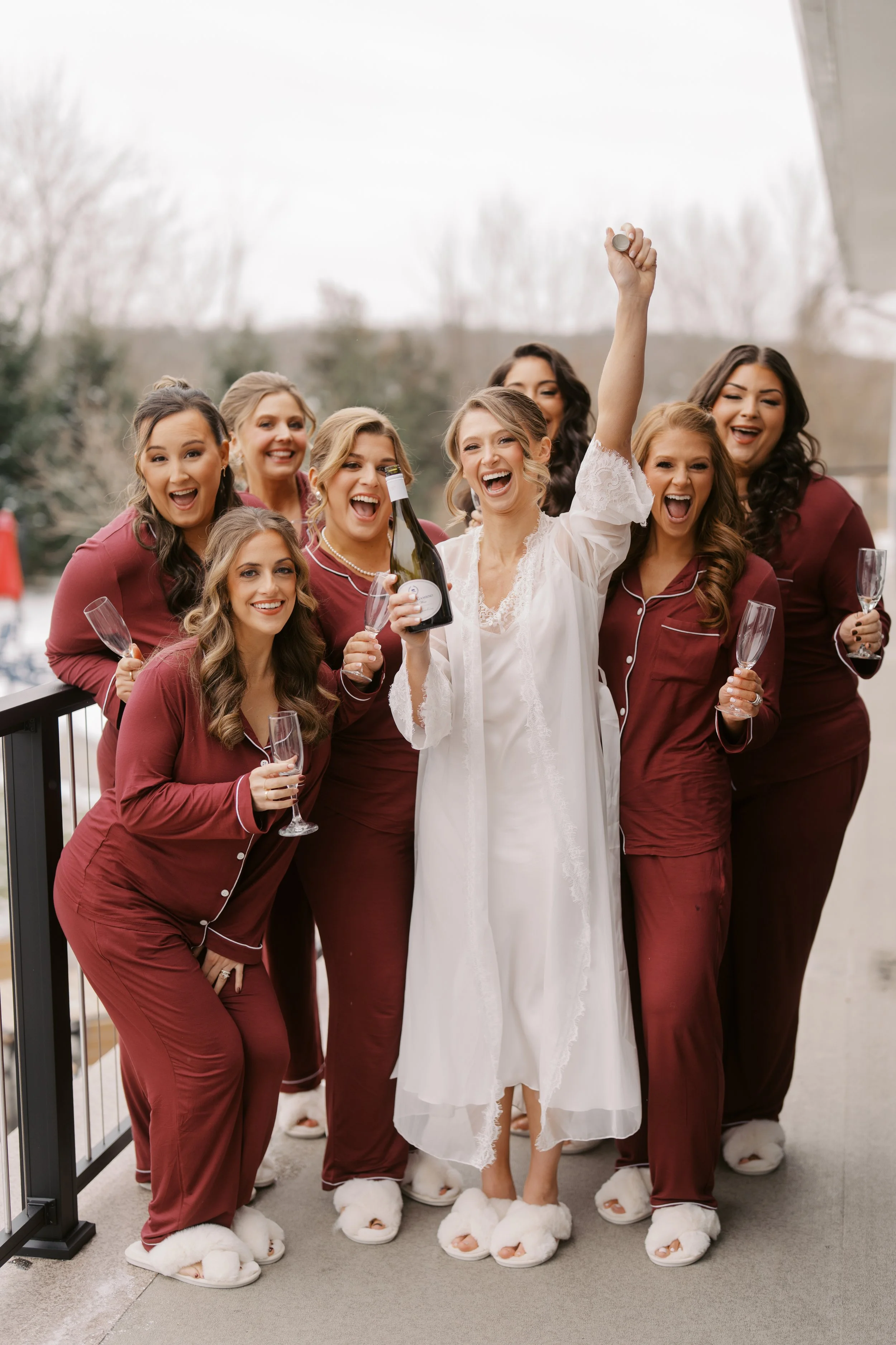 Bride and her bridesmaids popping a bottle of champagne on the deck outside of the bridal suite.