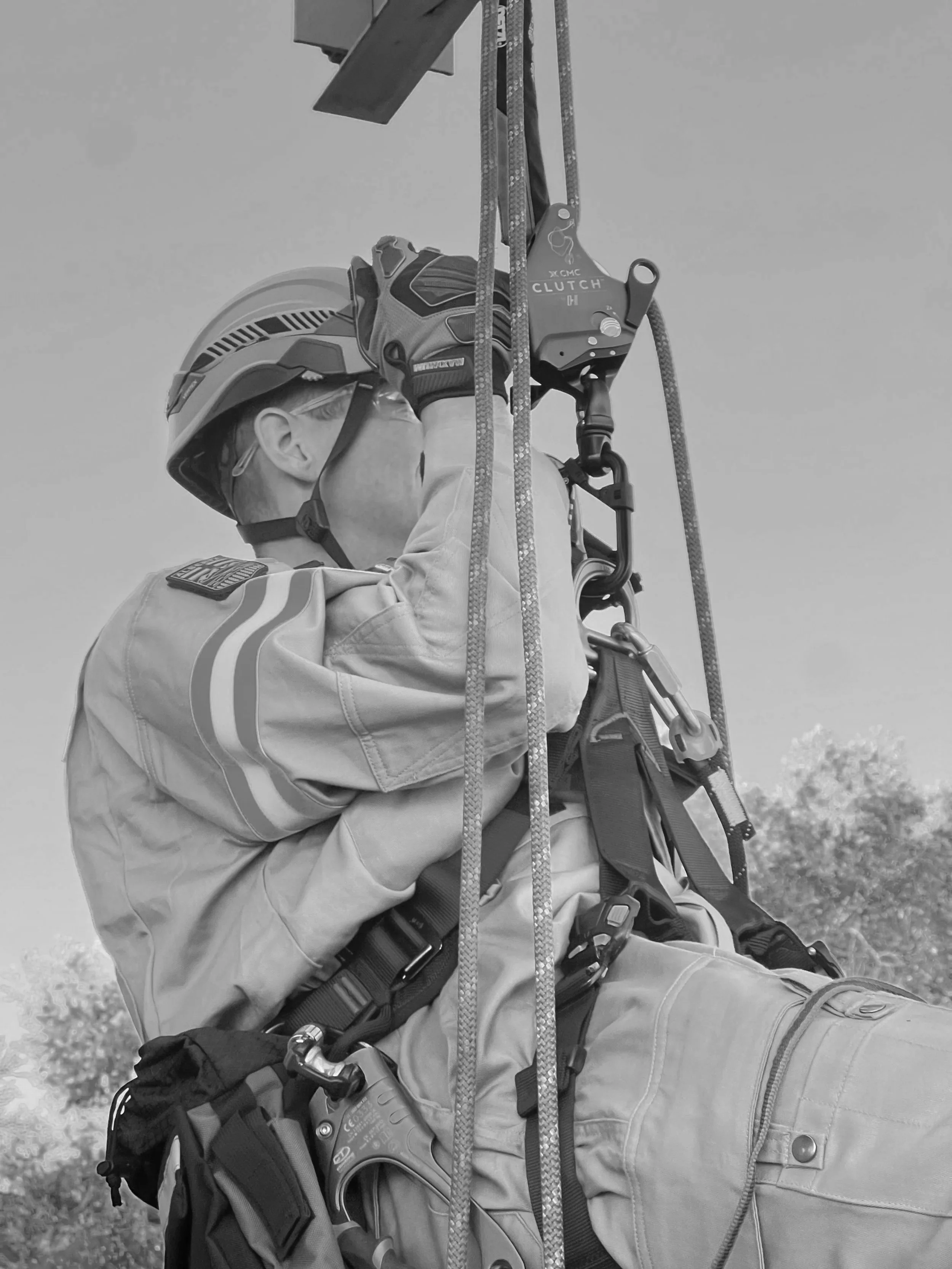 A worker in safety gear, including a helmet and gloves, using a harness and rope system for climbing or maintenance work.