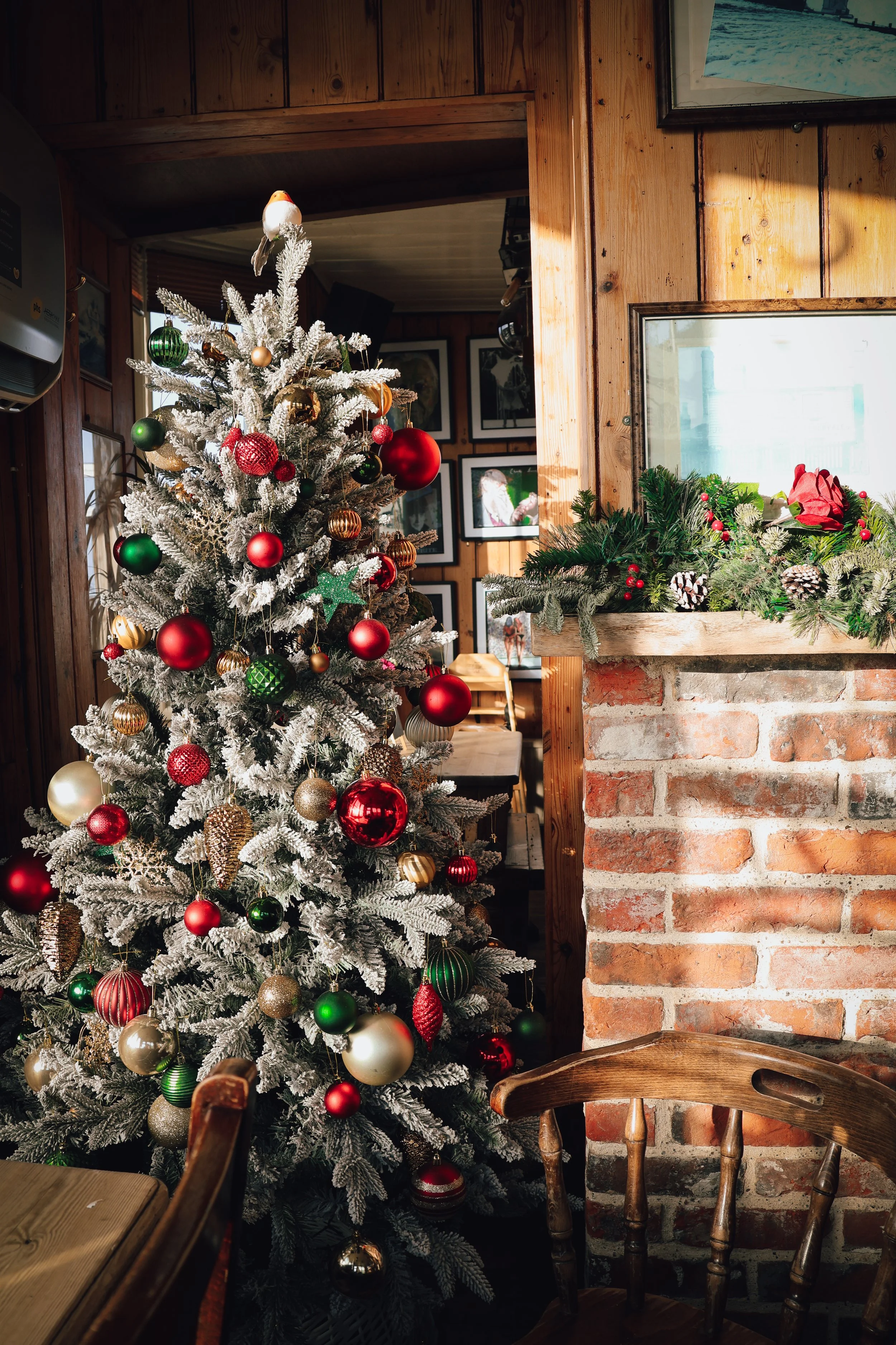 Decorated Christmas tree with red, gold, and green ornaments inside a cozy wooden room.
