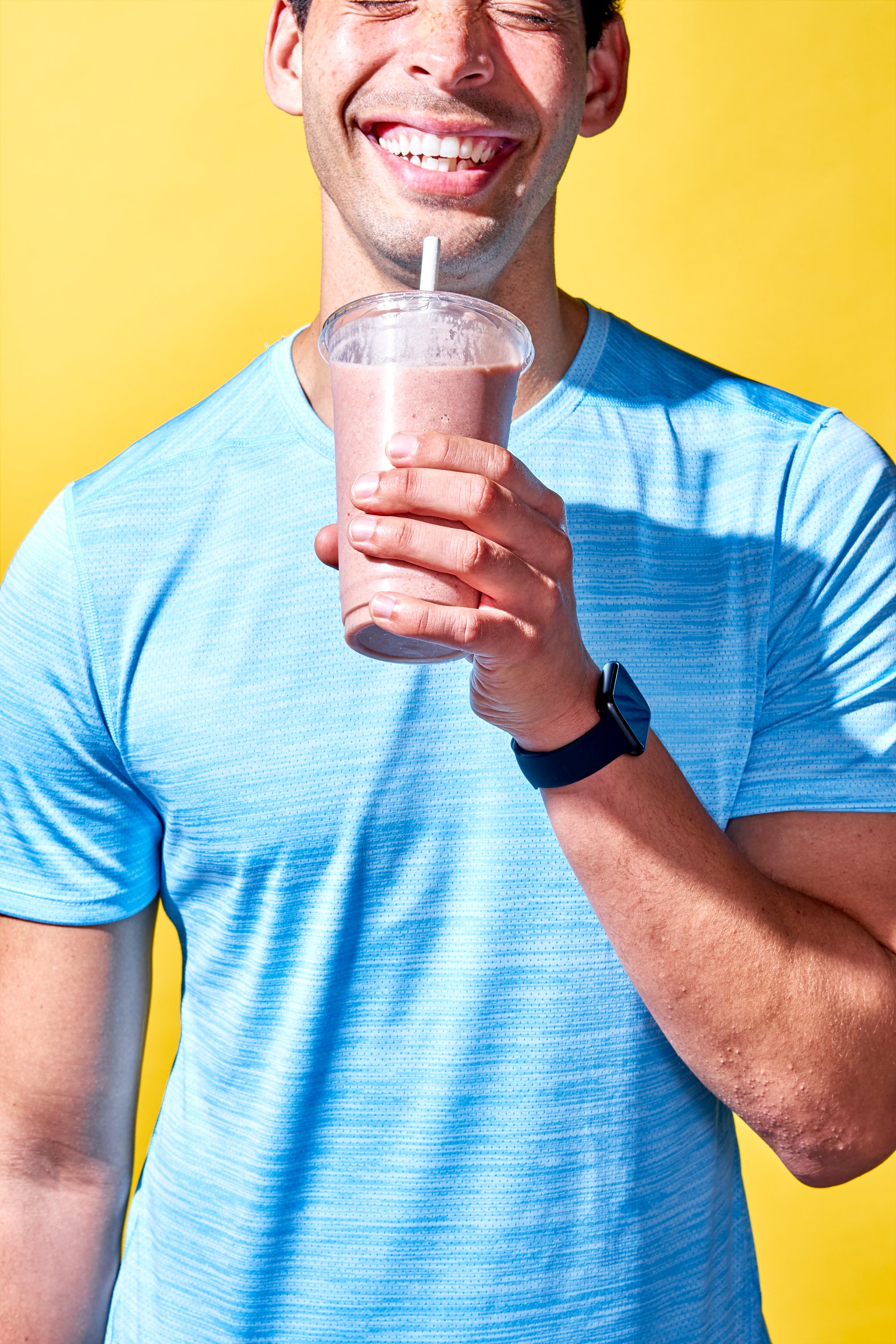 Professional lifestyle photography by Gold Sky Filmworks featuring a joyful man in blue sportswear with a strawberry smoothie, highlighted by a vibrant yellow backdrop, perfect for health and wellness campaigns.