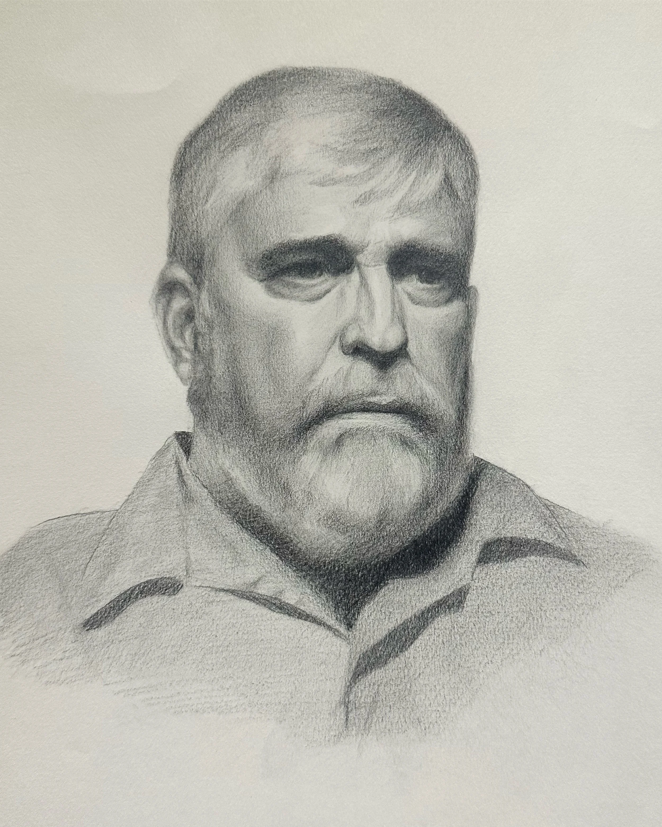 Close-up of a detailed graphite pencil drawing of a man's face, focusing on the eyes, nose, and beard, with a plain background.