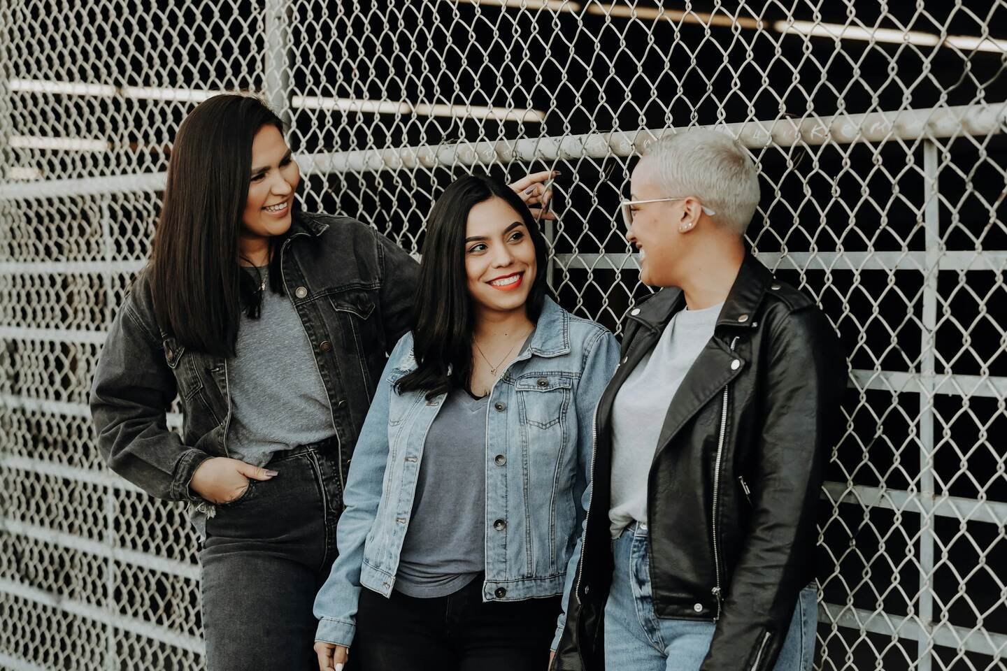 three women leaning against a fence smiling