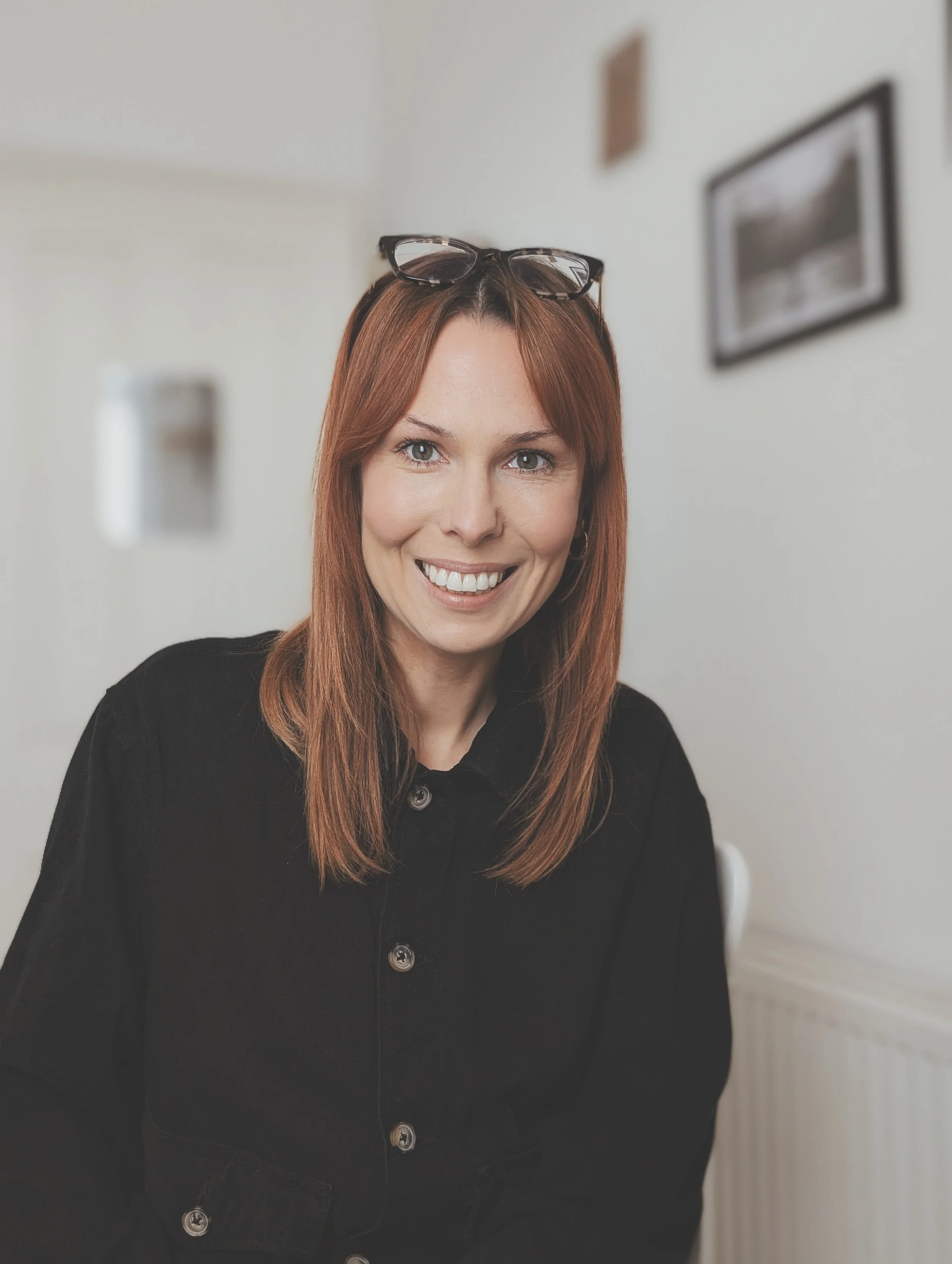 girl with copper hair wearing a black shirt smiling with glasses on head