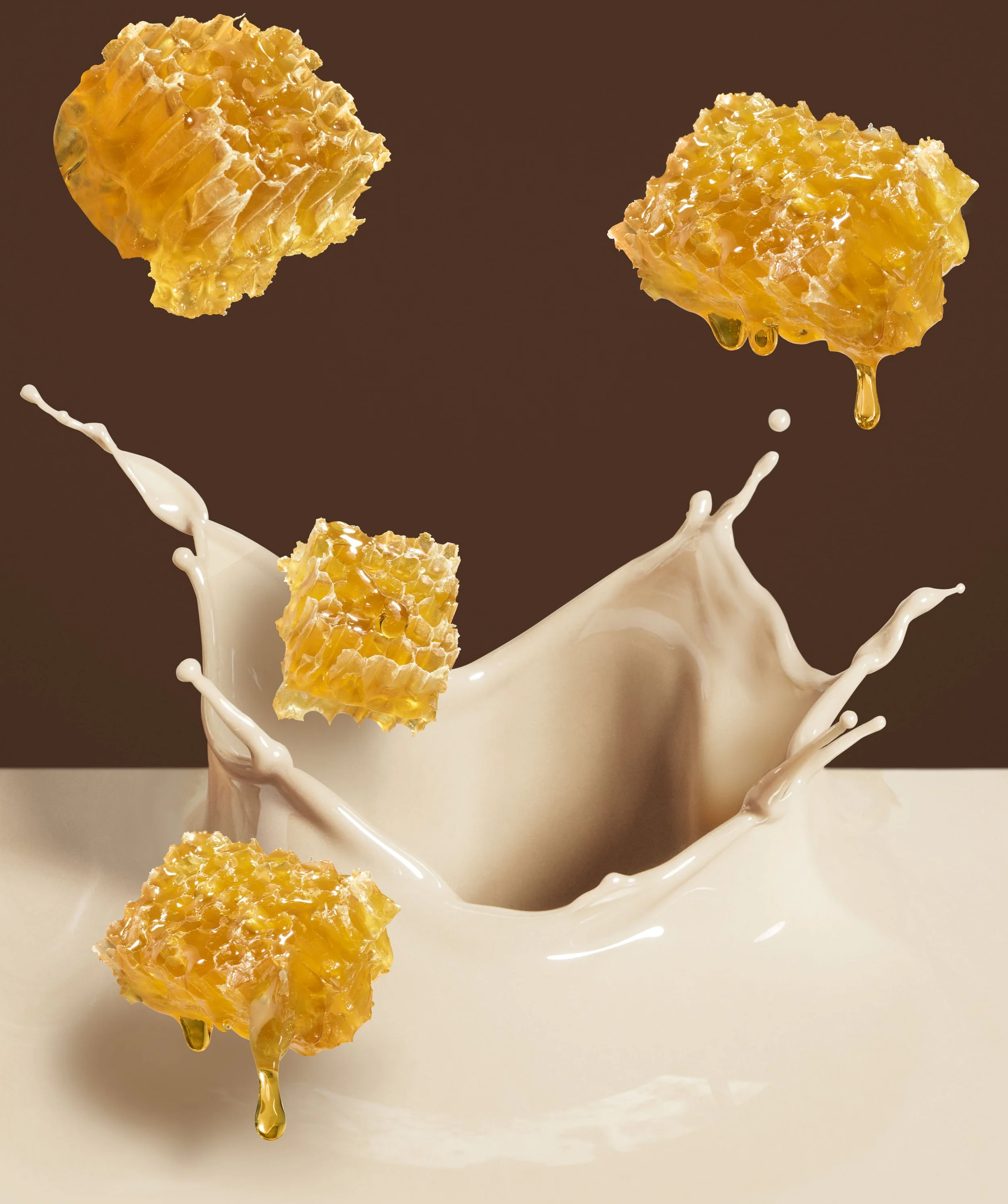 Close-up of honeycomb pieces falling into a splash of milk or cream against a brown background.