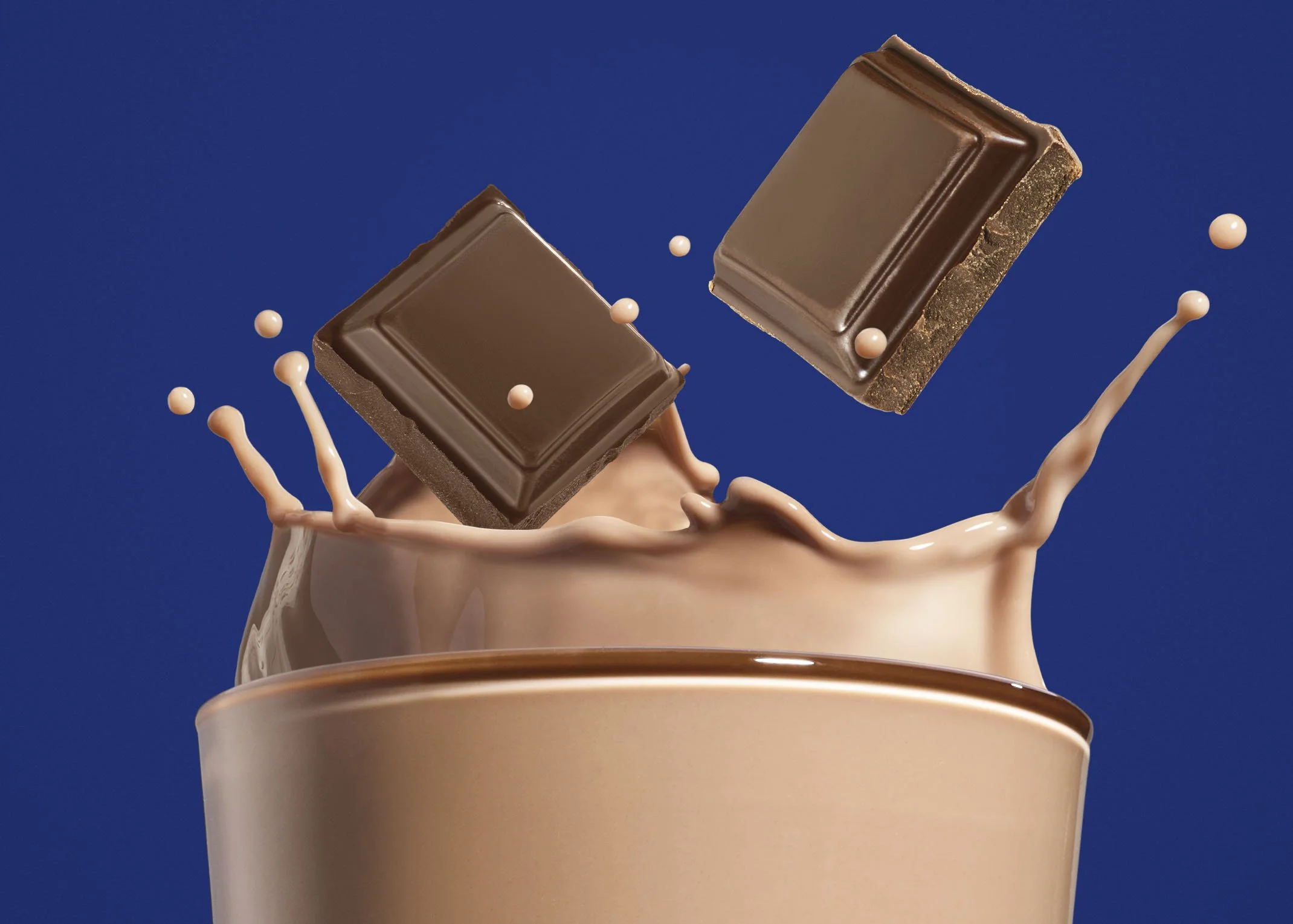 Chocolate pieces falling into a cup filled with chocolate milk or hot chocolate, with splash effects against a blue background.