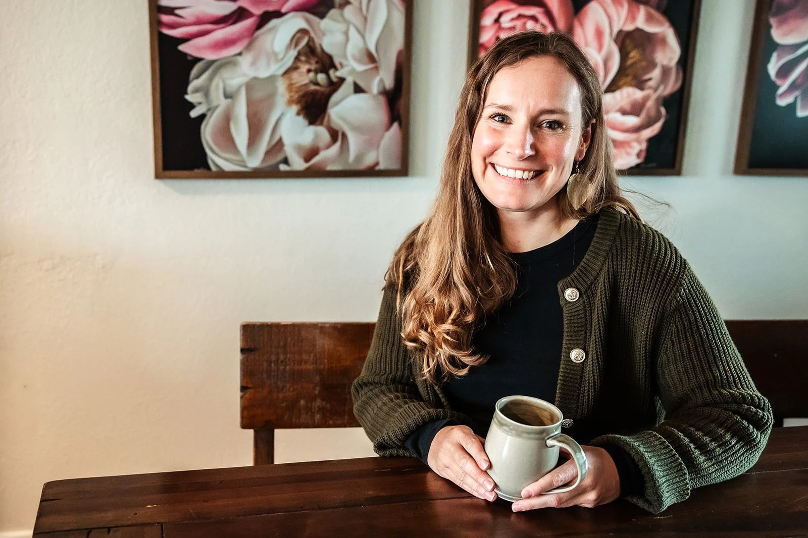 Karina Wenker, Nutritionist, sits at a table with a coffee mug in hand, smiles welcoming into the camera