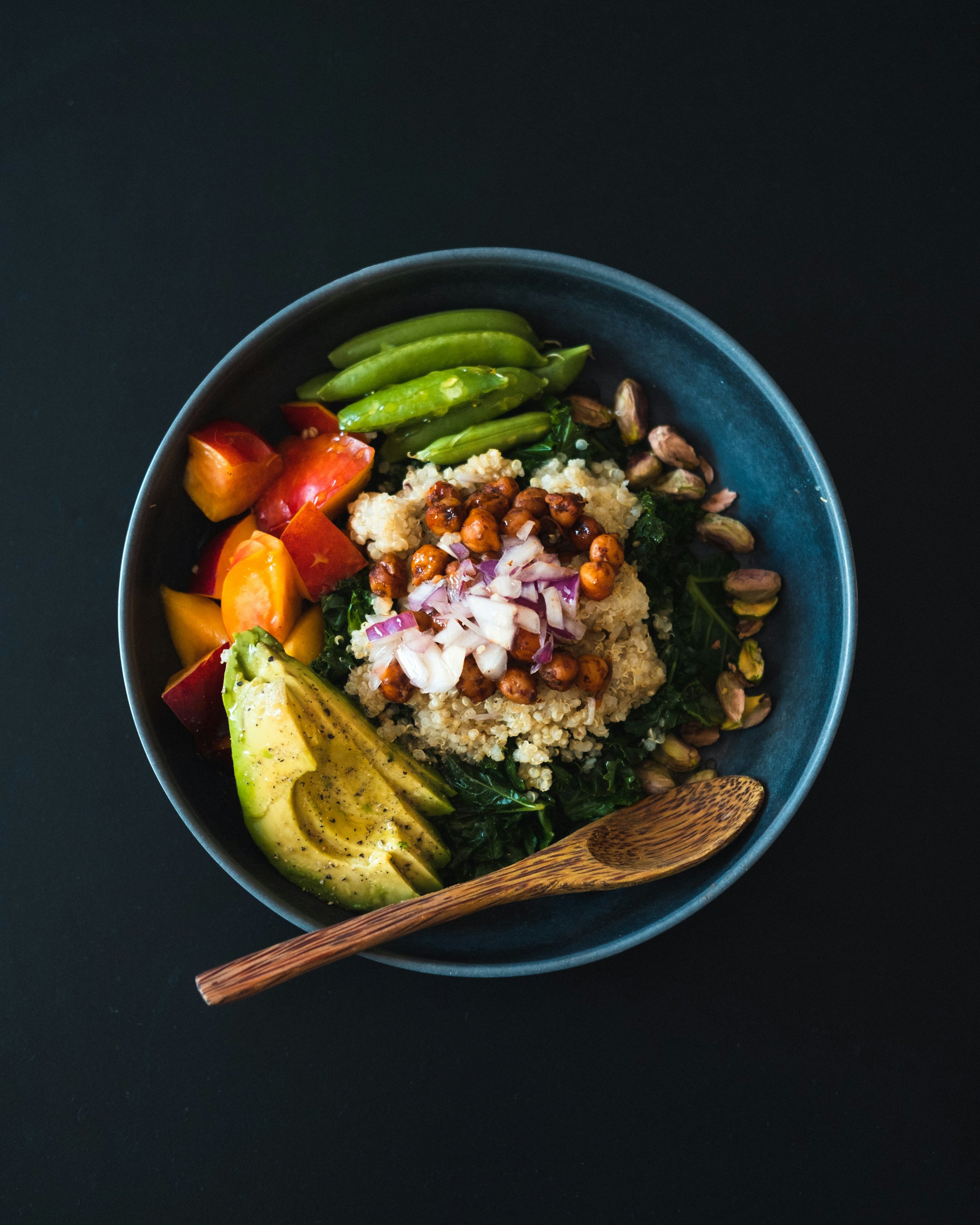 Blue bowl filled with nourishing food (quinoa, avocado, vegetables, legumes) and a wooden spoon