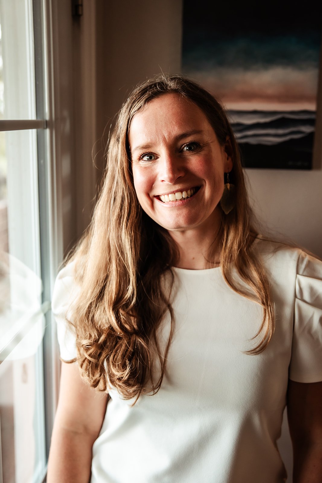 Karina, a Functional Nutritionist, stands near a window and smiles at the camera